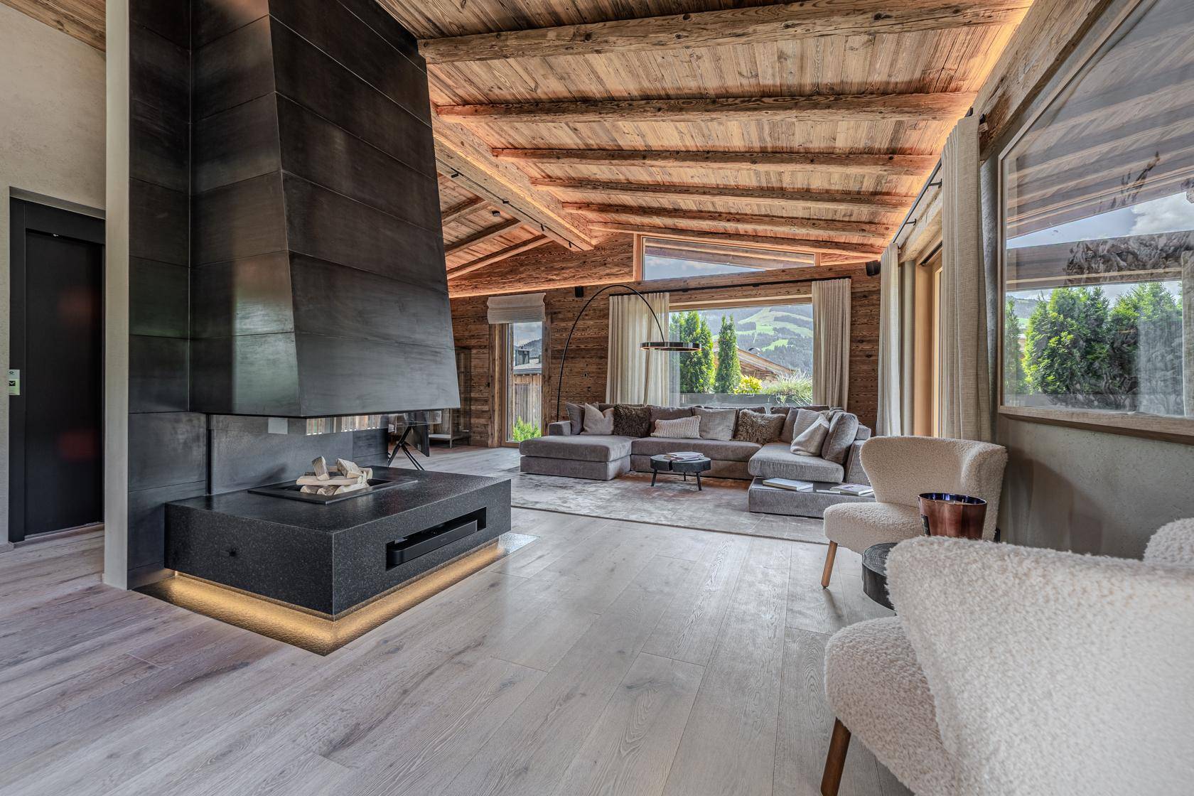 Gemütliches Wohnzimmer mit modernem Kamin, großem Sofa und weitem Blick auf die umliegende Berglandschaft.