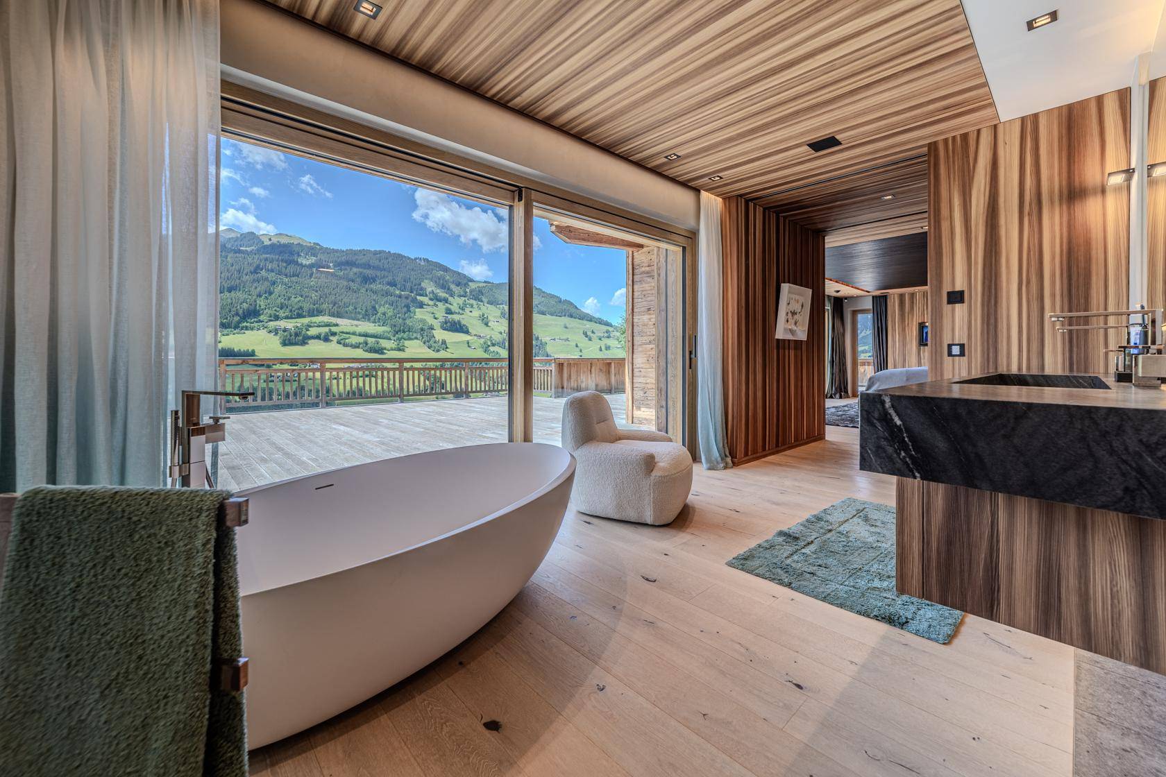 Luxuriöses Badezimmer mit freistehender Badewanne, Holzwänden und Panoramablick auf die Berge.