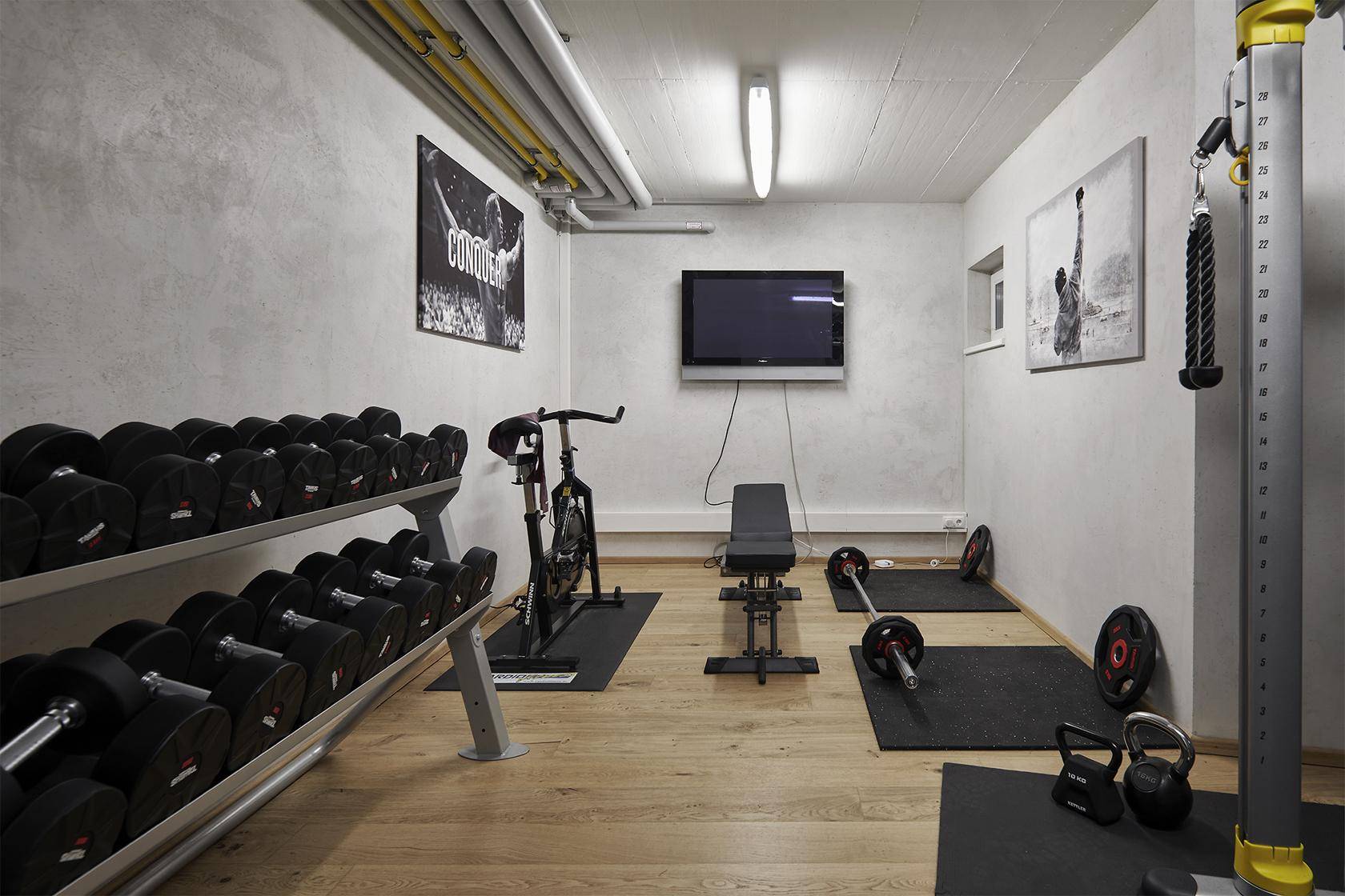 Gut ausgestatteter Fitnessraum mit Hanteln, Trainingsgeräten und Fernseher für Sportbegeisterte.