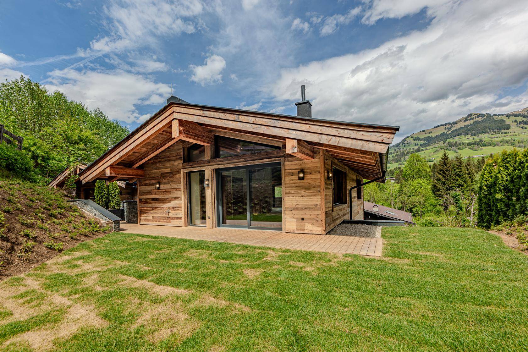 Charmantes Chalet mit Rasenfläche und Terrasse, umgeben von grüner Natur.