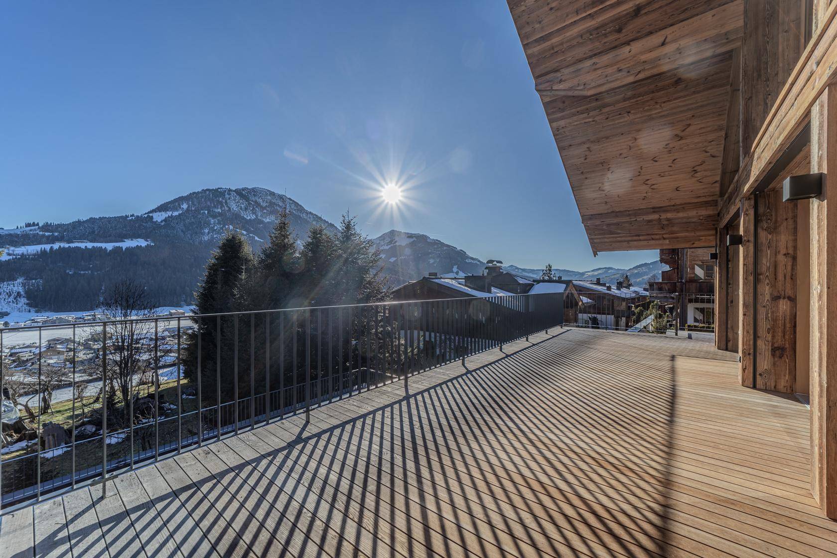 Große Holzterrasse mit Metallgeländer und sonnigem Blick auf die umliegende Berglandschaft.