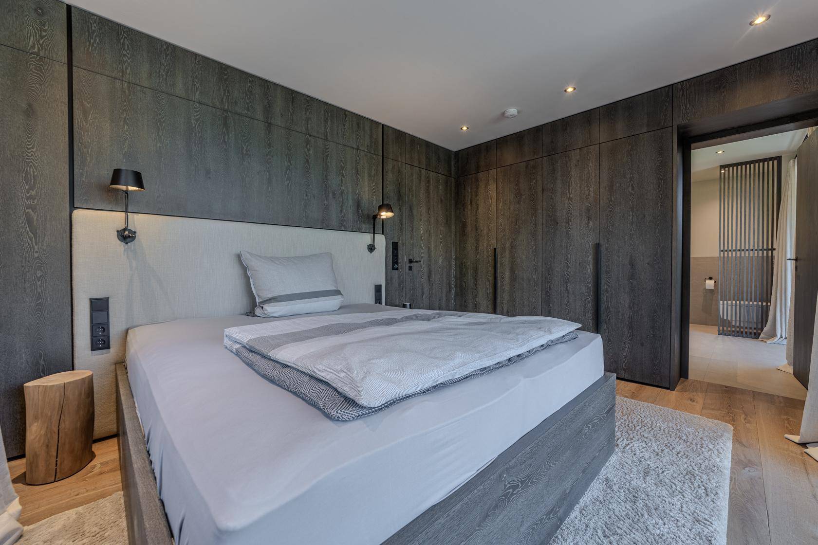 Gemütliches Schlafzimmer mit dunklen Holzwänden, Einbauschränken und modernem Bett.