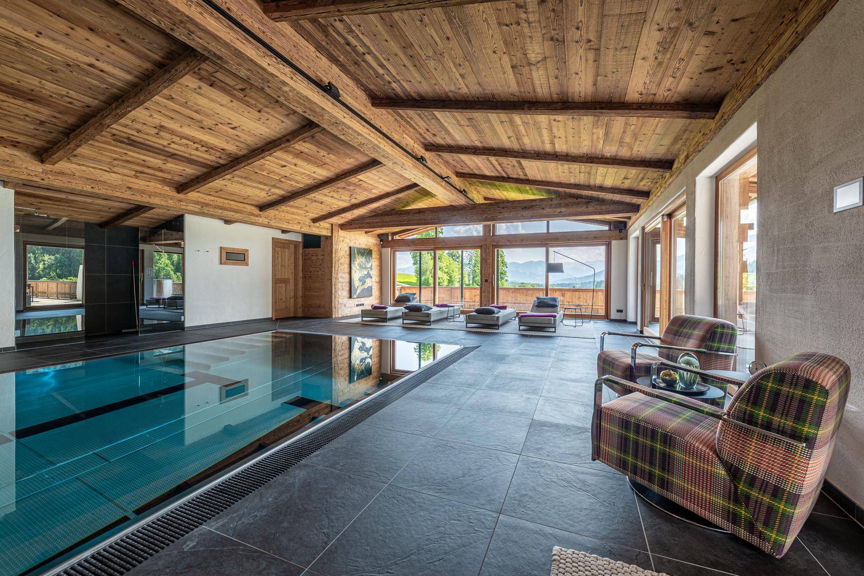 Heller Innenpoolbereich mit Liegestühlen, Holzbalkendecke und Panoramablick auf die Berge.
