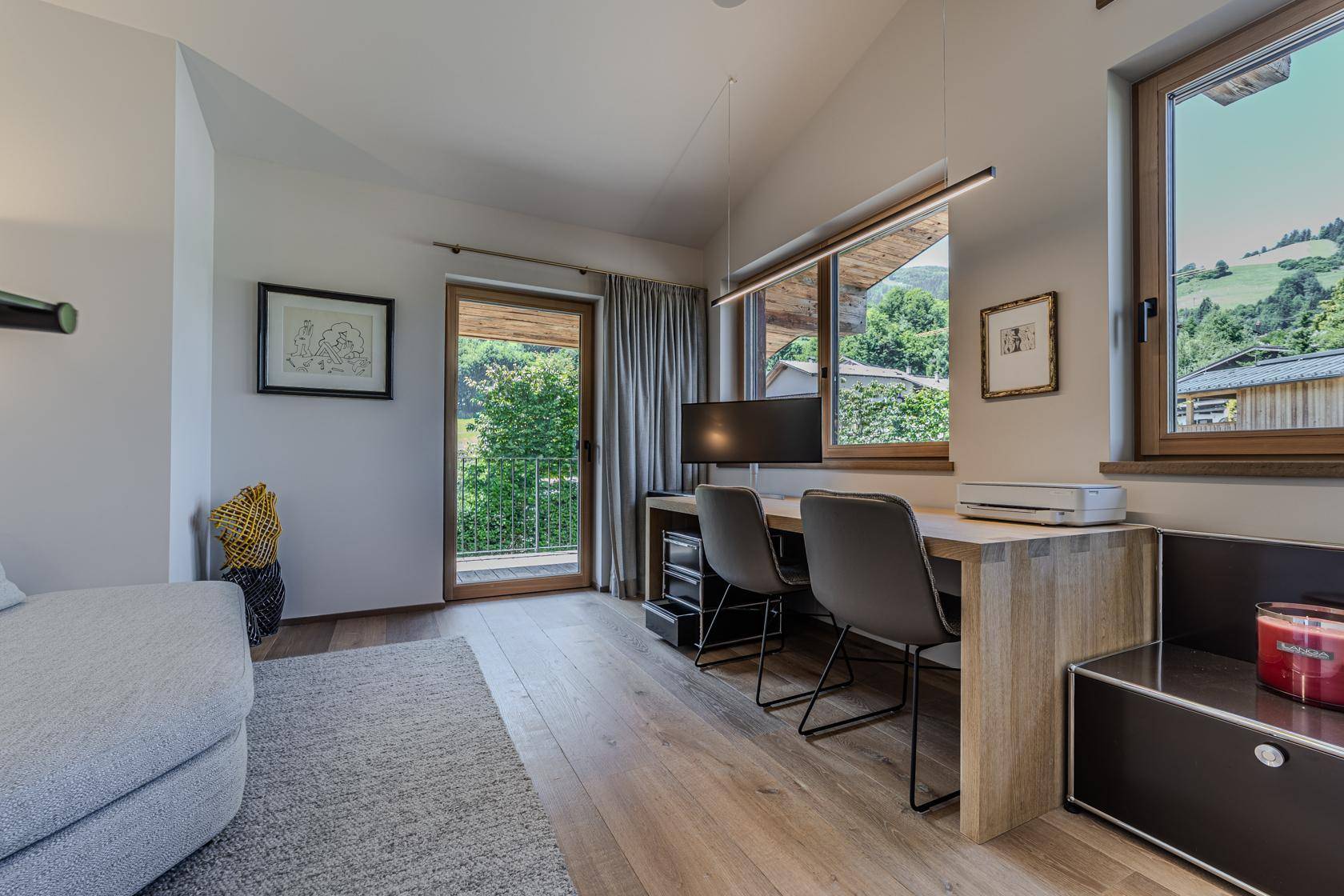 Helles Arbeitszimmer mit Holzboden, Schreibtisch und großen Fenstern mit Blick auf die grüne Umgebung.