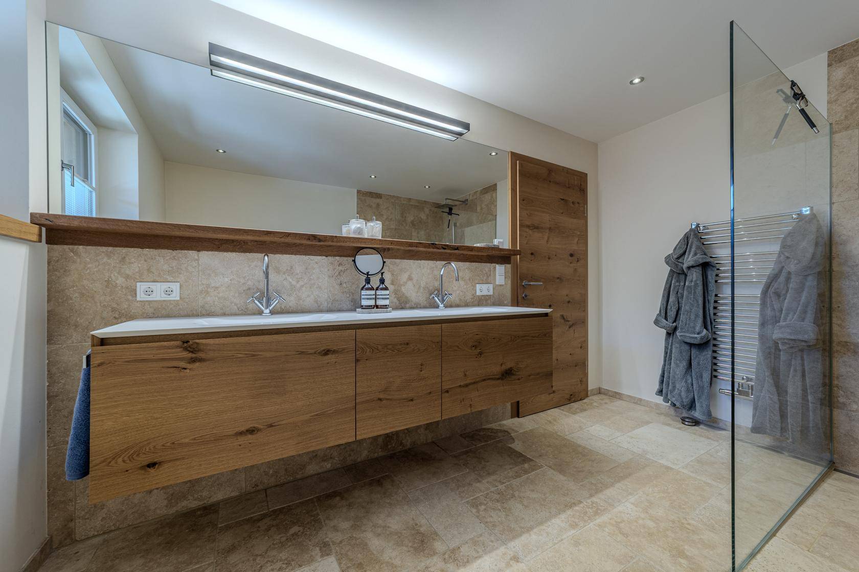 Elegantes Badezimmer mit Doppelwaschbecken, großem Spiegel und geräumiger ebenerdiger Dusche.