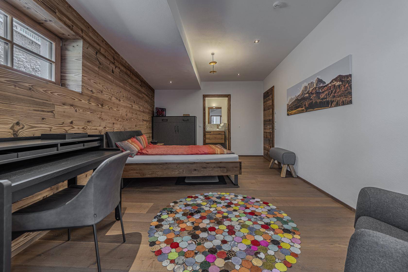 Stilvolles Schlafzimmer mit Holzwand, Schreibtisch und Blick auf das angrenzende Badezimmer.