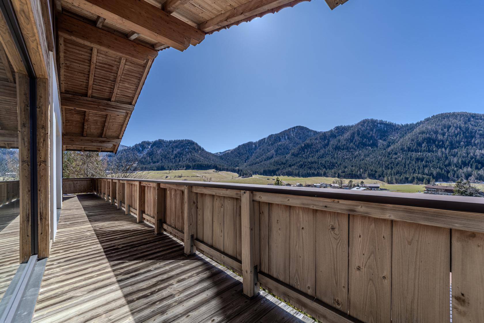 Langer Holzbalkon mit weitem Blick auf die umliegende Berglandschaft und viel Sonne.