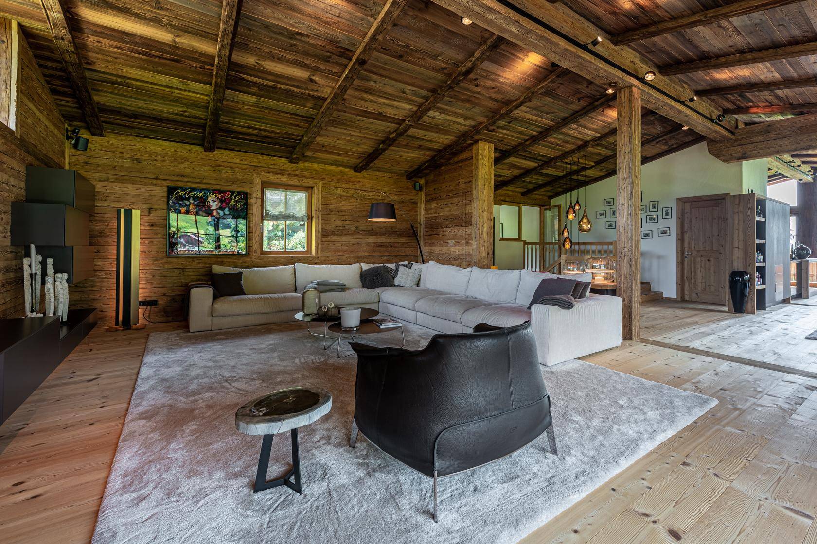 Helles Wohnzimmer mit Holzbalkendecke, großem Sofa und Blick auf die grüne Umgebung.