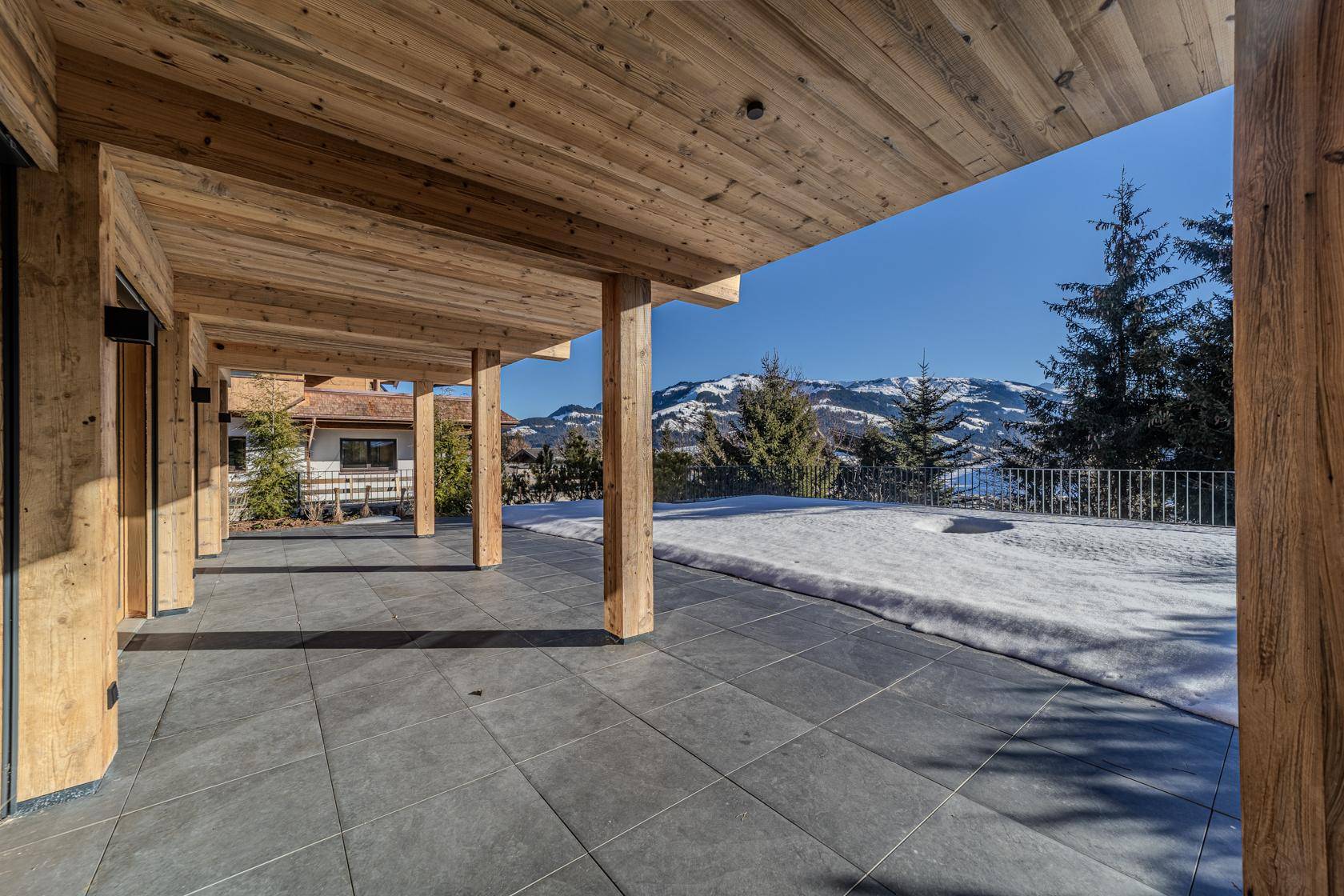 Überdachte Terrasse mit Fliesenboden und weitem Blick auf die schneebedeckten Berge.