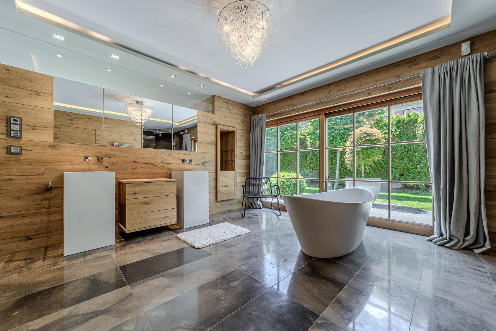Elegantes Badezimmer mit freistehender Badewanne, Doppelwaschbecken und Blick in den Garten.