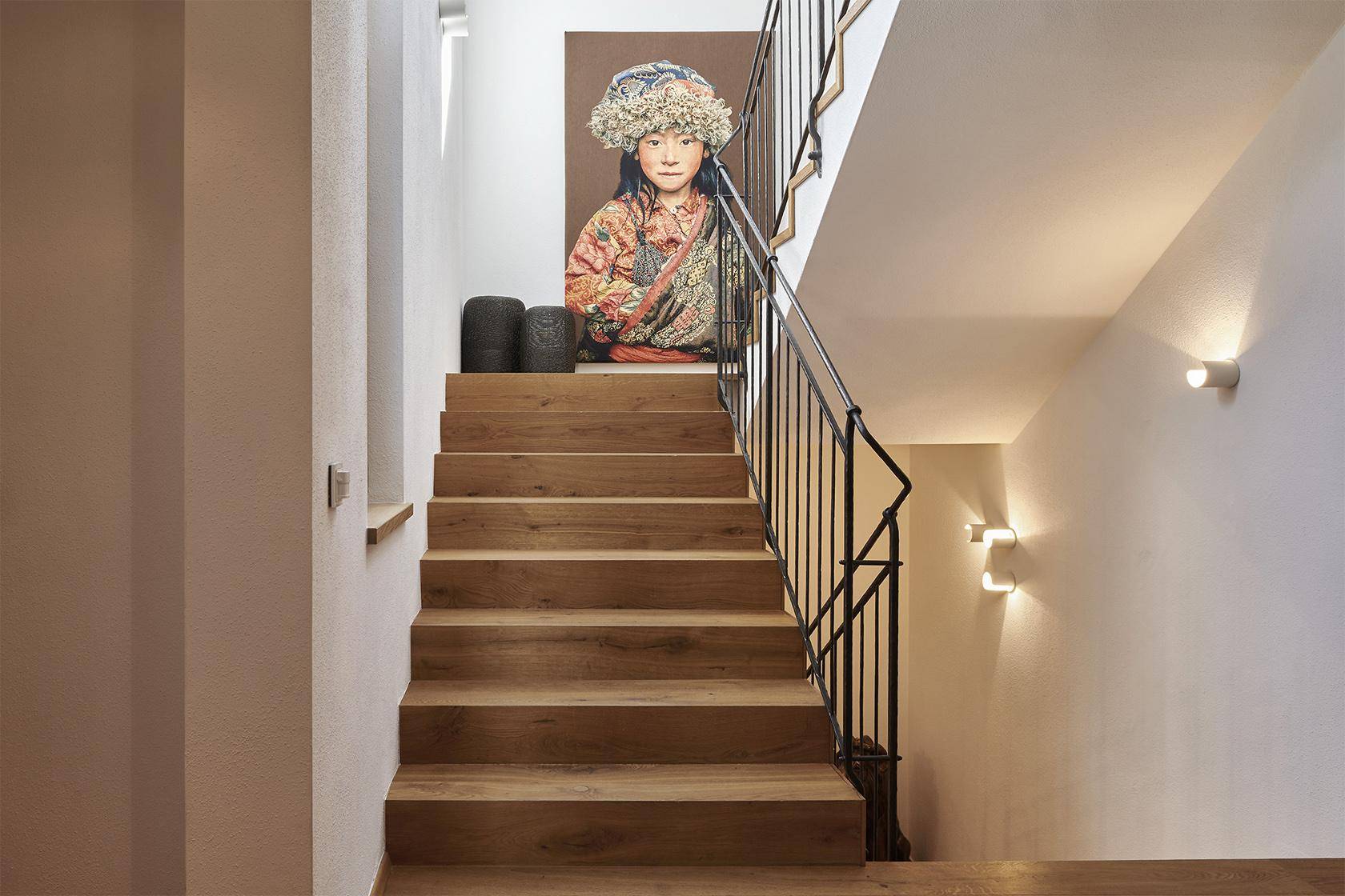 Heller Flur mit Holztreppe, Metallgeländer und dekorativem Kunstwerk an der Wand.