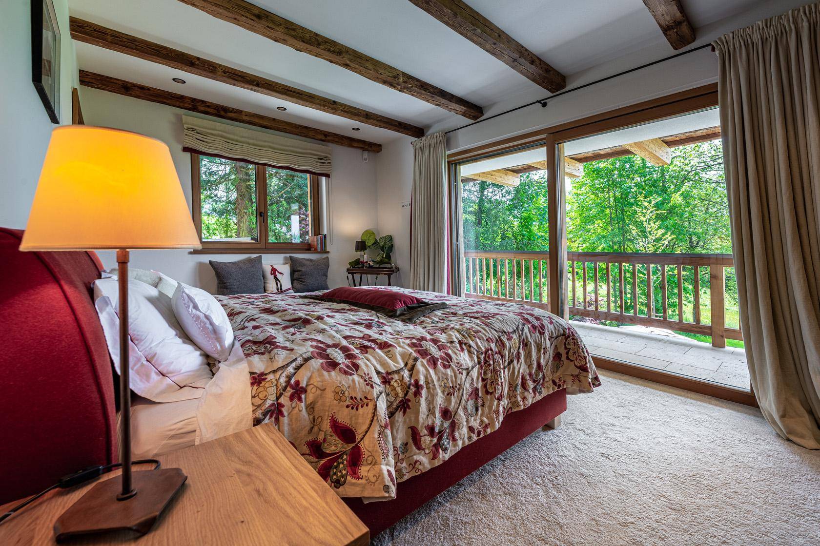 Helles Schlafzimmer mit Teppichboden, Holzbalken und direktem Zugang zum Balkon.