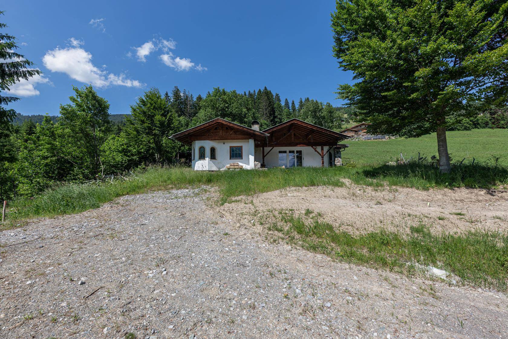 Traditionelles Haus in ländlicher Umgebung mit grünen Wiesen und bewaldeten Hügeln im Hintergrund.