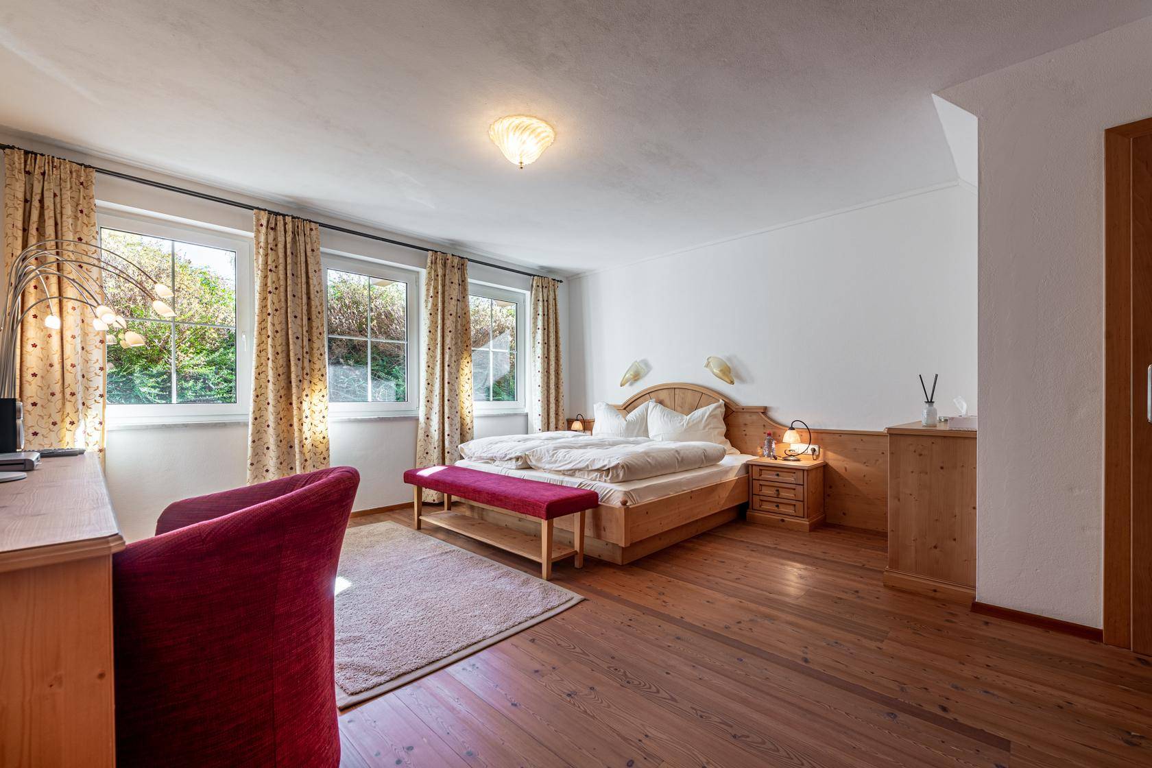 Geräumiges Schlafzimmer mit Doppelbett, Holzboden und mehreren Fenstern für viel Licht.