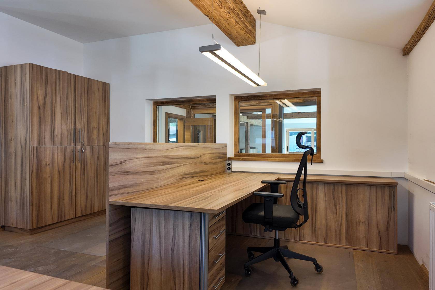 Heller Büroraum mit Holzmöbeln, Schreibtisch und großen Fenstern, die viel Tageslicht hereinlassen.