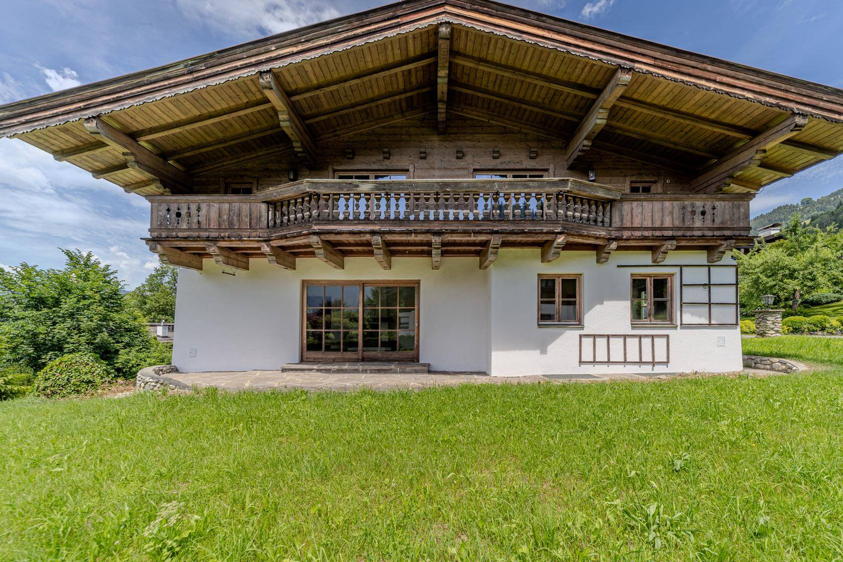 Detailansicht der Hausfassade mit traditionellem Holzbalkon und großen Fenstern zum Garten.