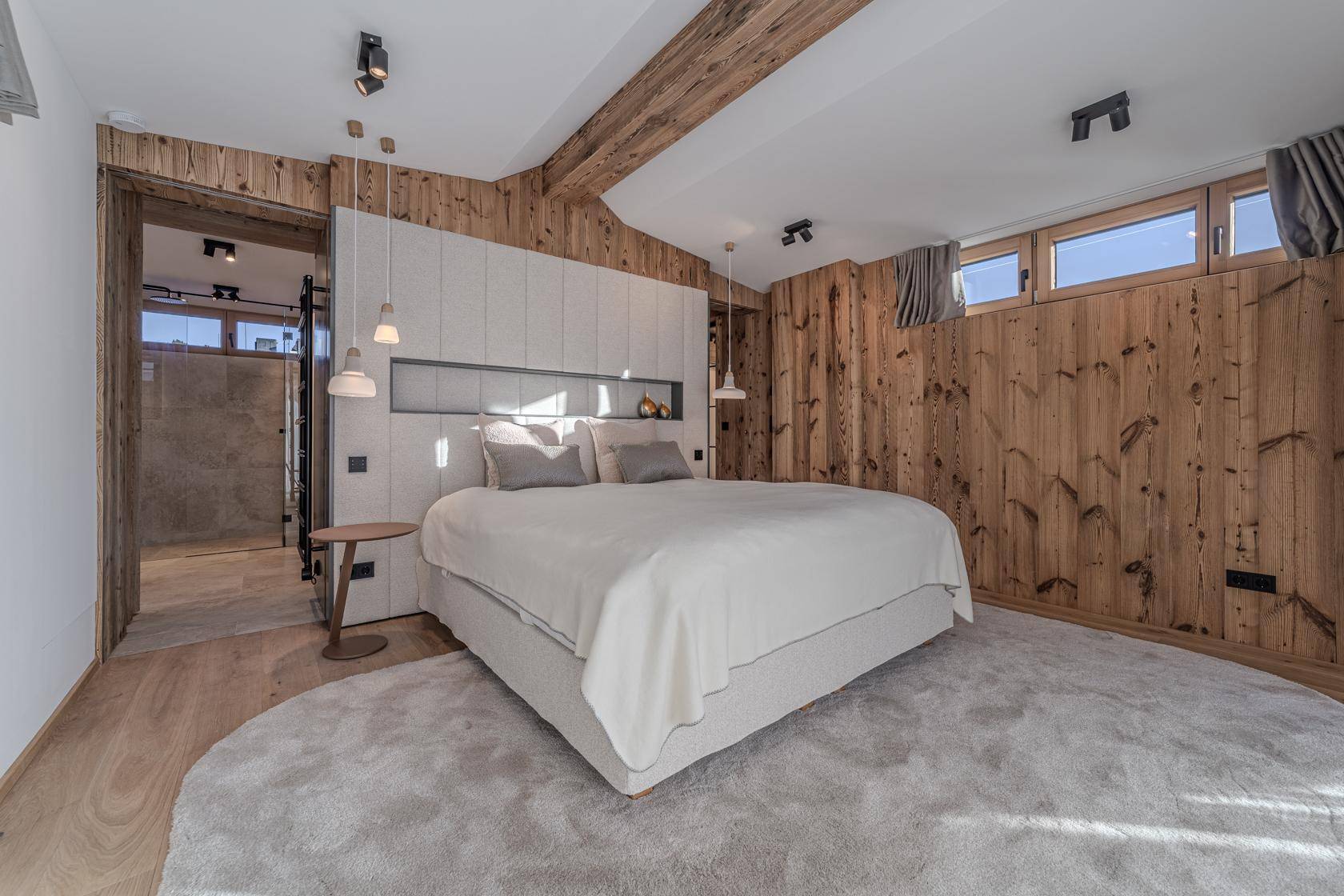 Helles Schlafzimmer mit Doppelbett, Holzwänden und indirekter Beleuchtung unter Holzbalken.