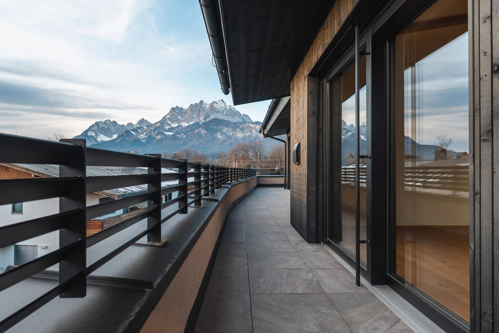 Lange, geschwungene Terrasse mit Fliesenboden und Geländer, die einen weiten Bergblick bietet.
