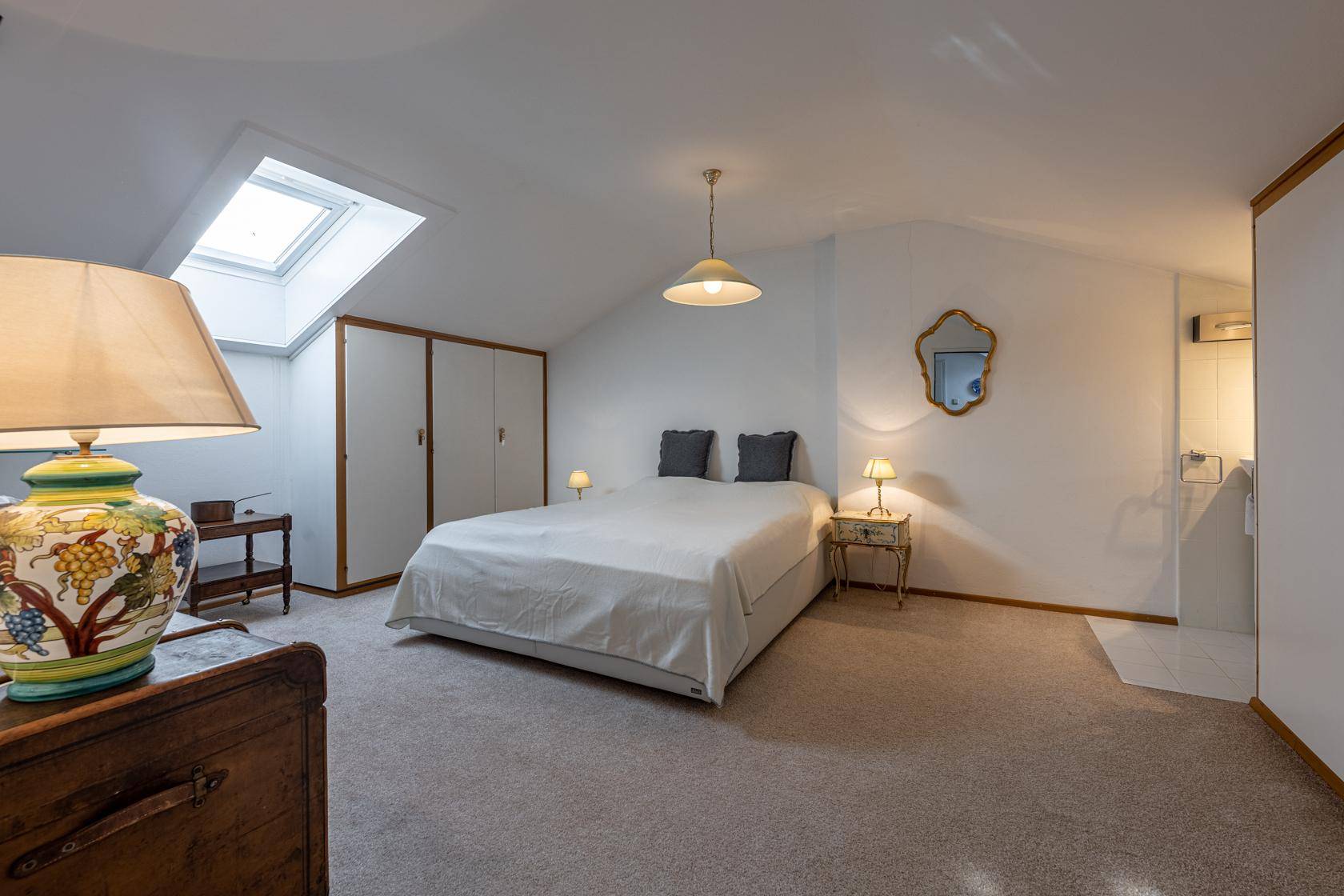Helles Schlafzimmer im Dachgeschoss mit Dachfenster, schrägen Wänden und Teppichboden.