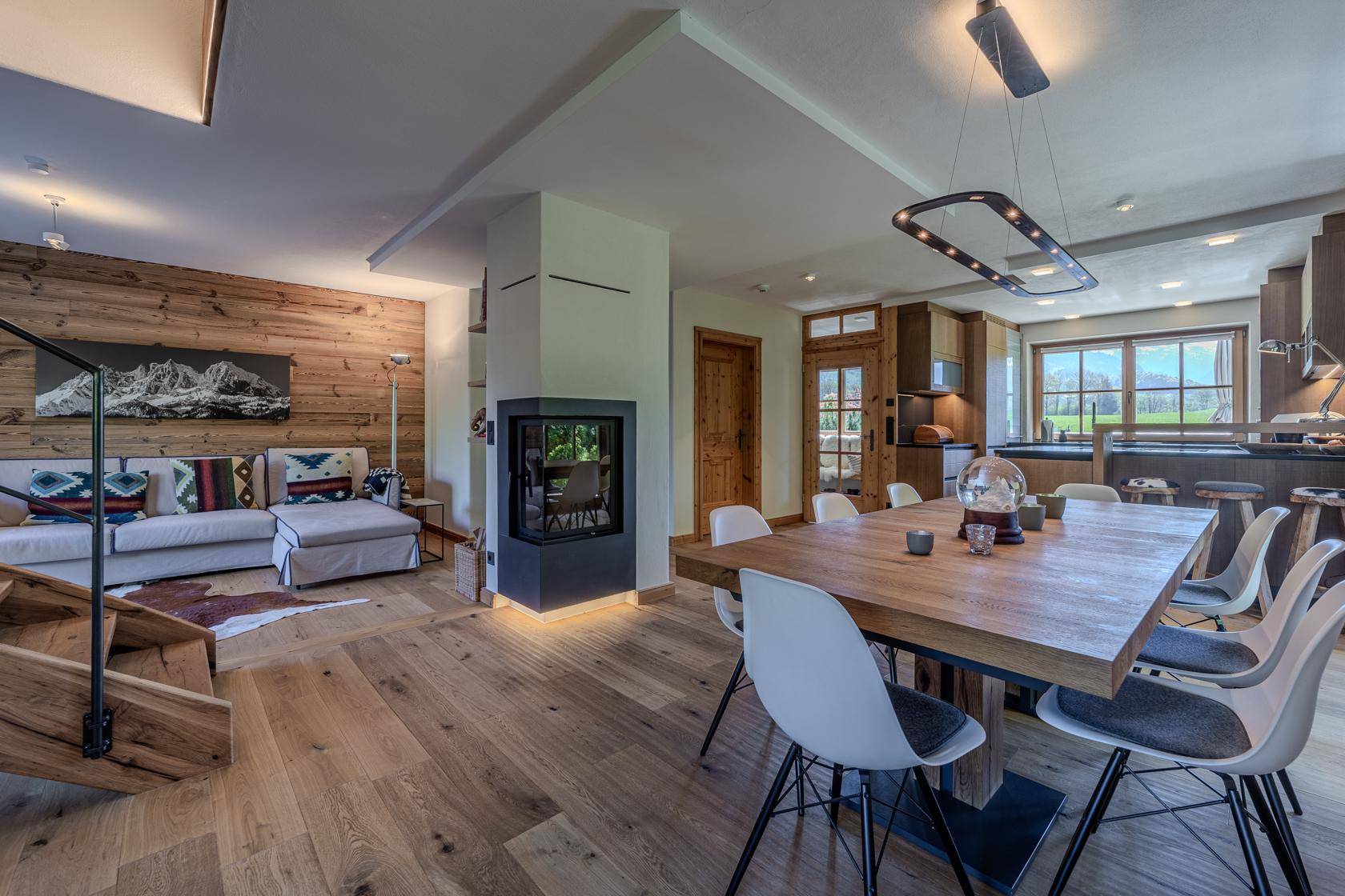 Gemütlicher Wohn-Essbereich mit Kamin, Holzwand und Zugang zur Küche.