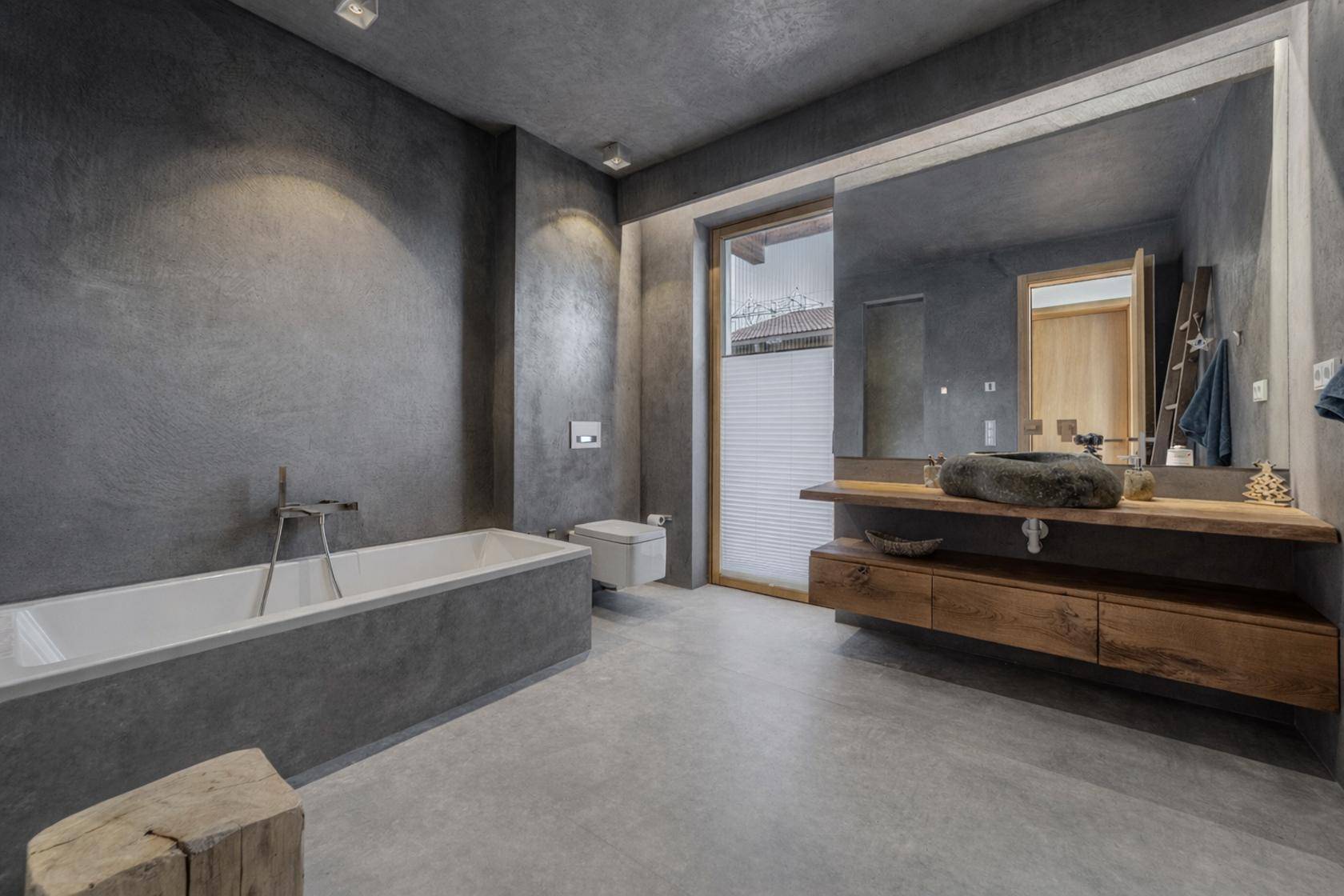 Modernes Badezimmer mit Betonoptik, Badewanne und stilvollem Holzwaschtisch.
