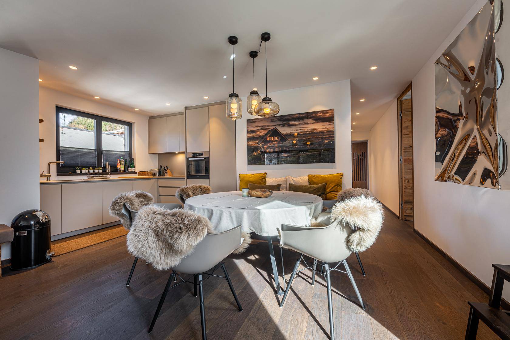 Moderne Küche mit integriertem Essbereich, Holzboden und stilvollen Pendelleuchten.