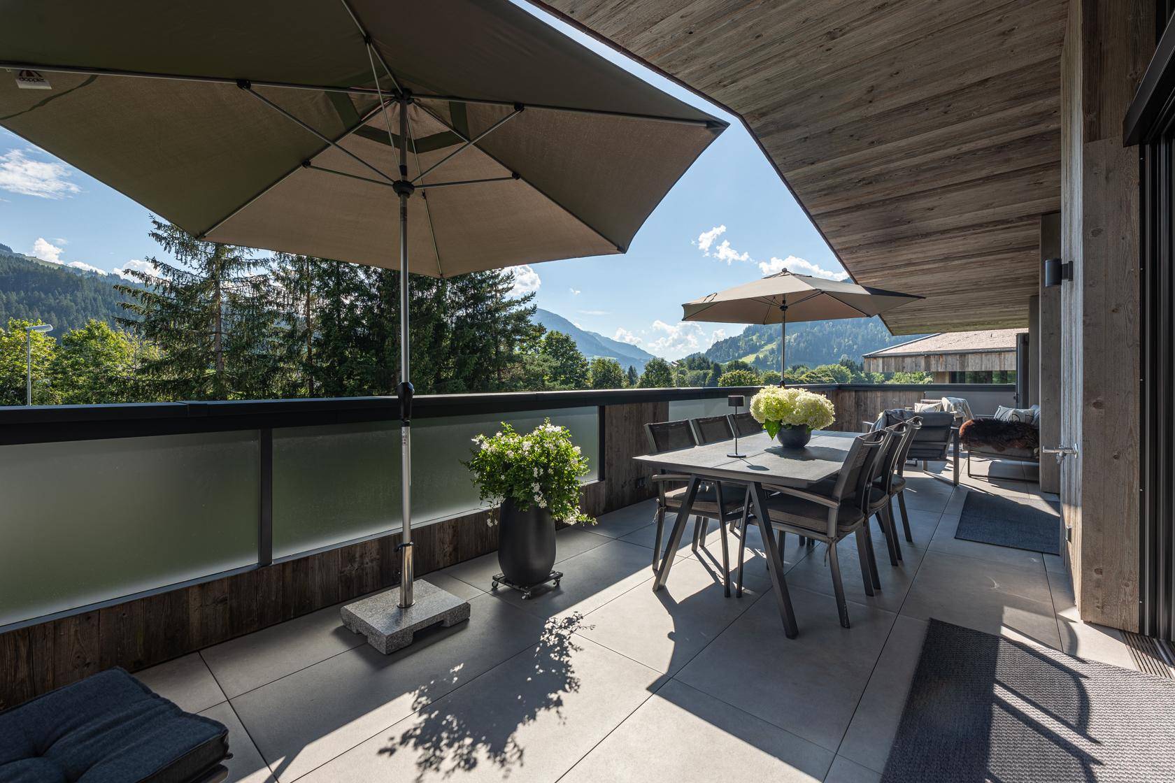 Geräumige Außenterrasse mit Esstisch, Sonnenschirmen und Panoramablick auf die Alpen.