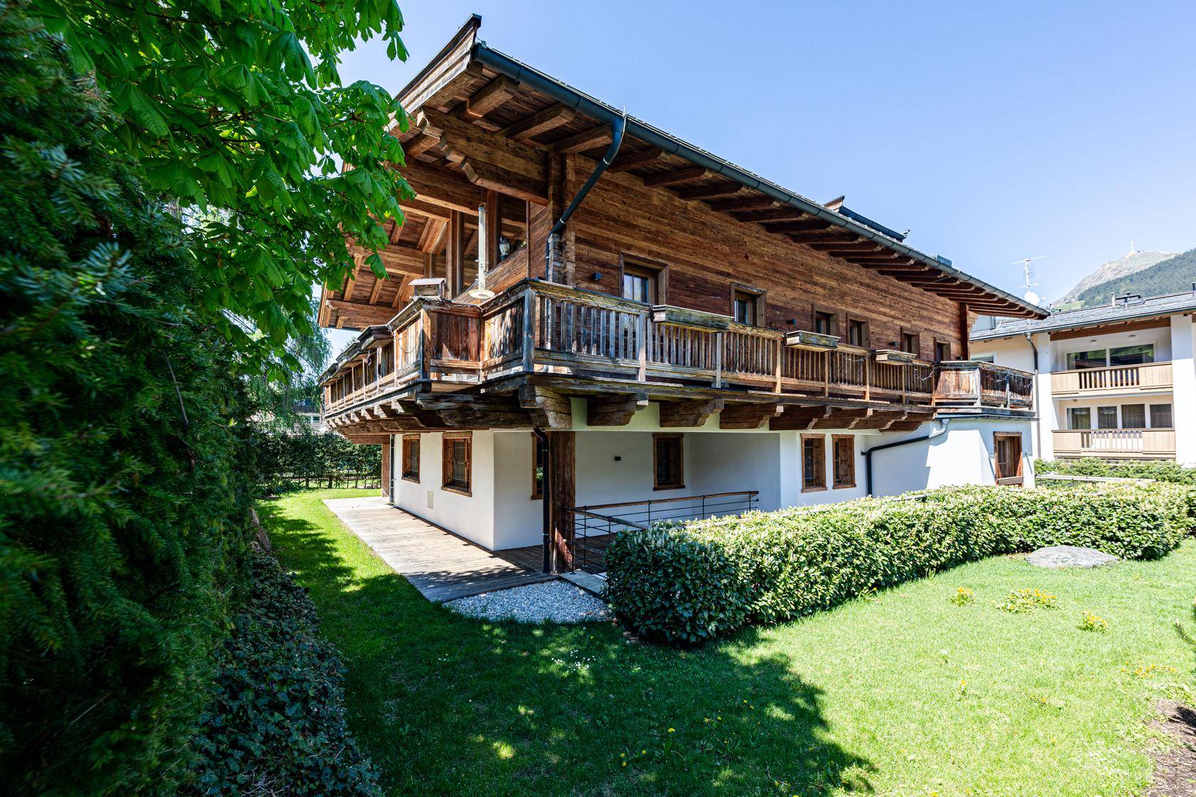 Traditionelles Holzchalet mit Balkonen und gepflegtem Gartenbereich in alpiner Umgebung.