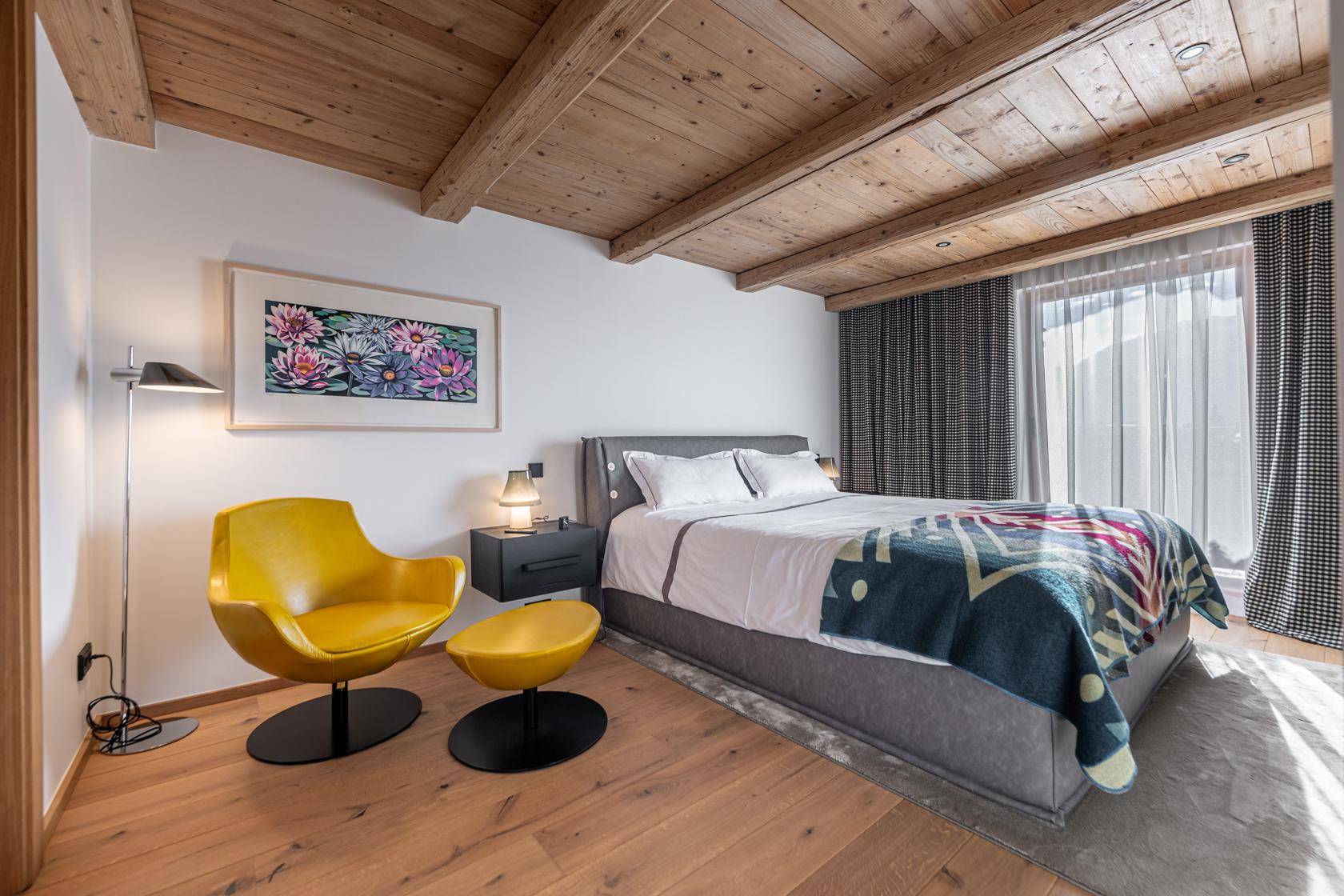 Modernes Schlafzimmer mit Holzbalkendecke, Holzboden und gelbem Sessel, hell und stilvoll eingerichtet.