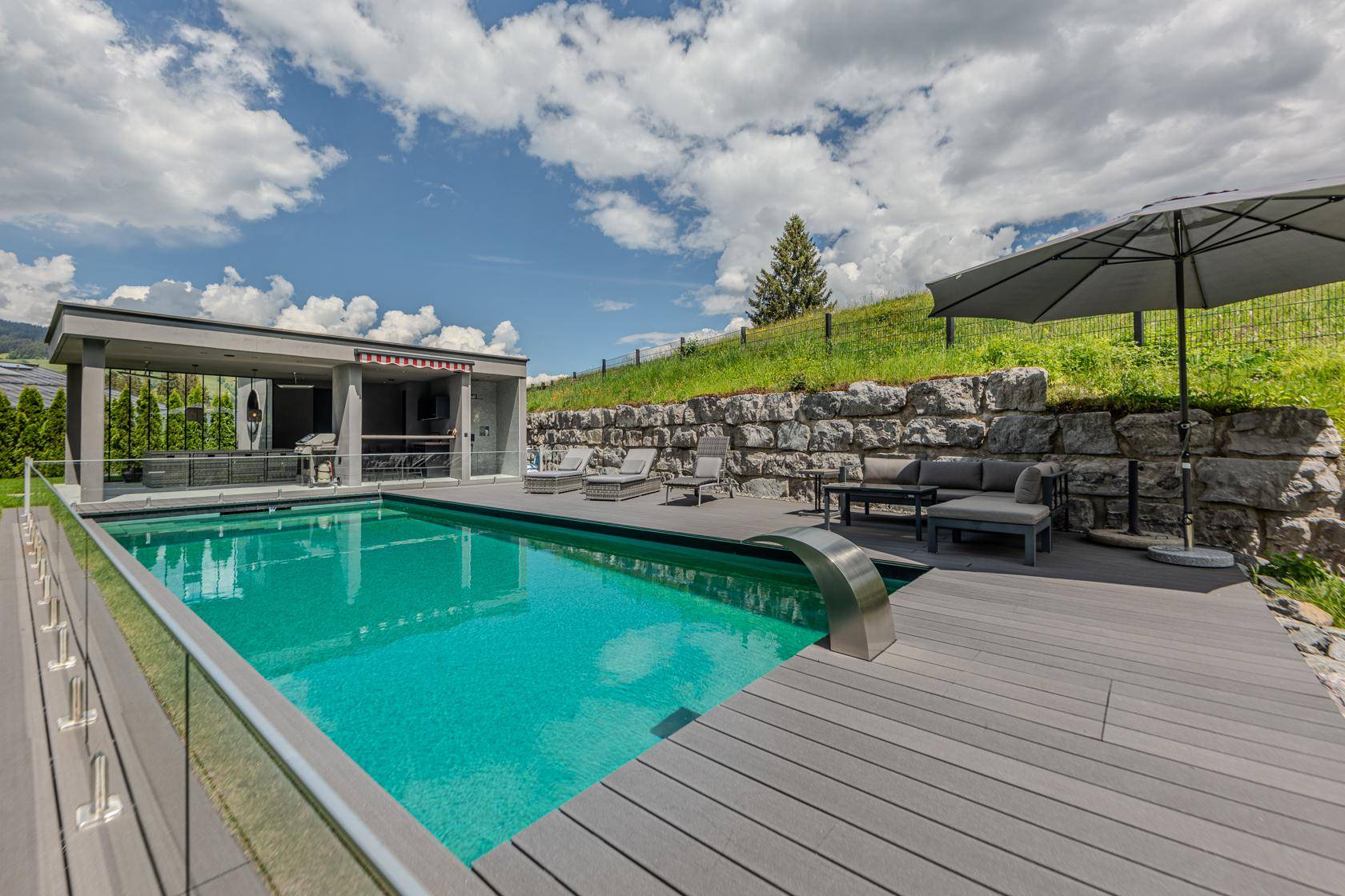 Exklusiver Poolbereich mit Holzdeck, Liegestühlen und gemütlicher Outdoor-Lounge.