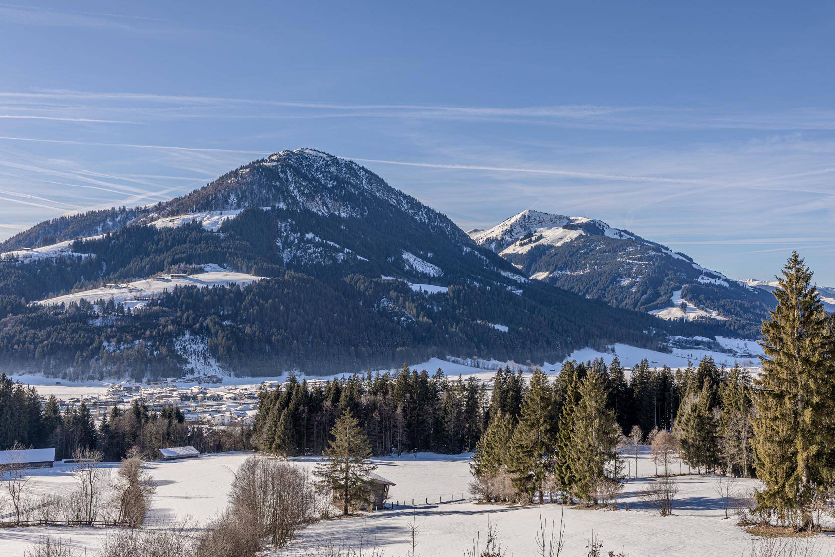 Weitläufige Winterlandschaft mit schneebedeckten Bergen und Wäldern unter blauem Himmel.