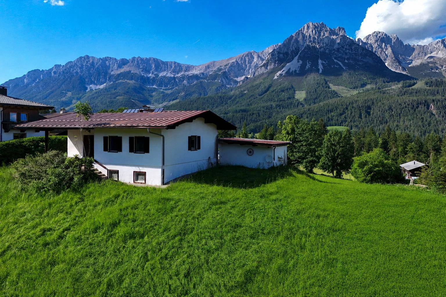 Freistehendes Haus auf einem grünen Hügel mit traditioneller Architektur und beeindruckendem Alpenpanorama.
