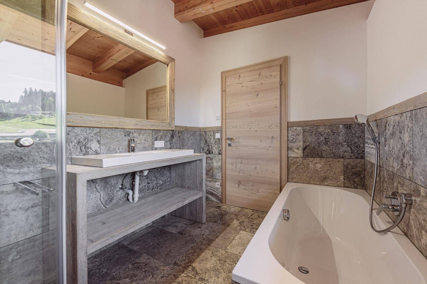 Modernes Badezimmer mit Badewanne, Waschtisch und Natursteinfliesen.