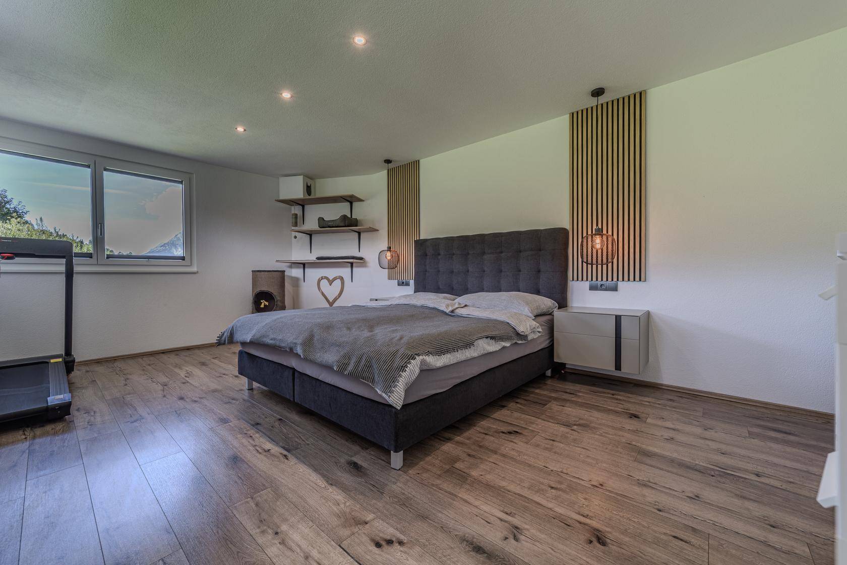 Geräumiges Schlafzimmer mit Doppelbett, Holzboden und Fenster mit Blick ins Grüne.