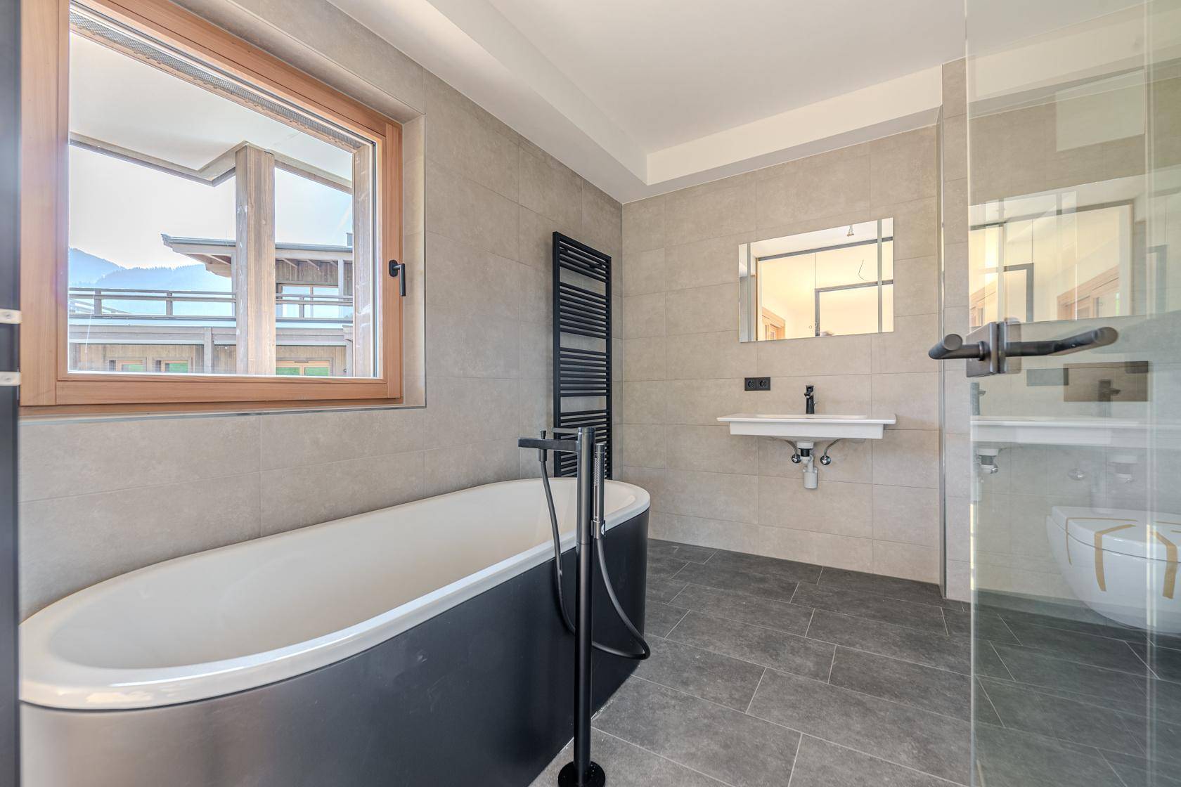 Modernes Badezimmer mit grauen Fliesen, freistehender Badewanne und begehbarer Dusche.