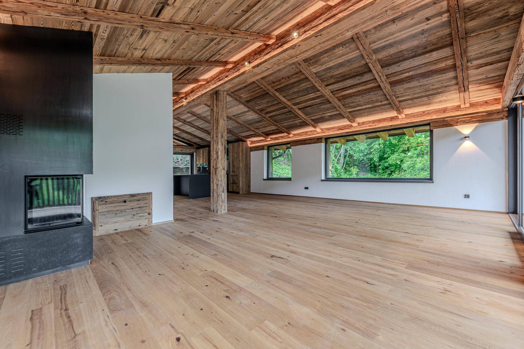 Geräumiger Wohnbereich mit Holzbalkendecke, Kamin und großen Fenstern zur Natur.