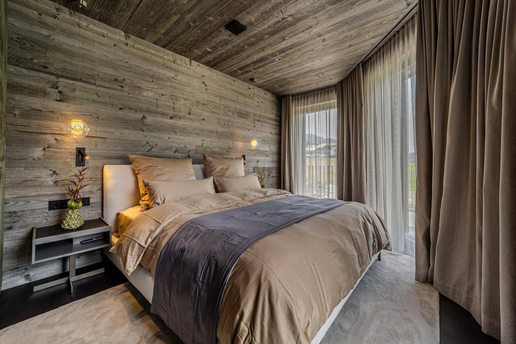 Gemütliches Schlafzimmer mit Holzwänden, großem Bett und Zugang zu einem Balkon mit Bergblick.