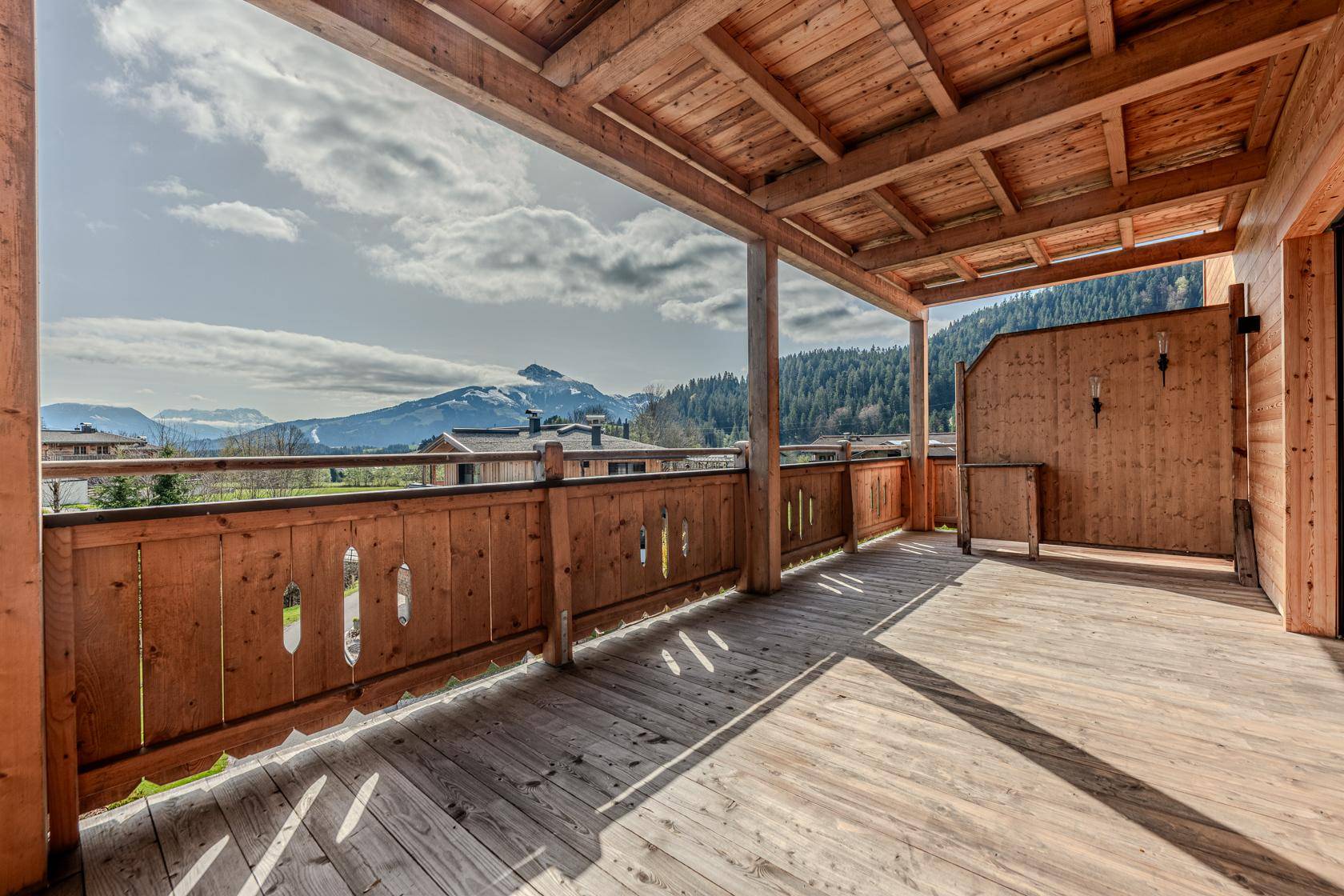 Großer überdachter Holzbalkon mit Panoramablick auf die Berge und die grüne Umgebung.