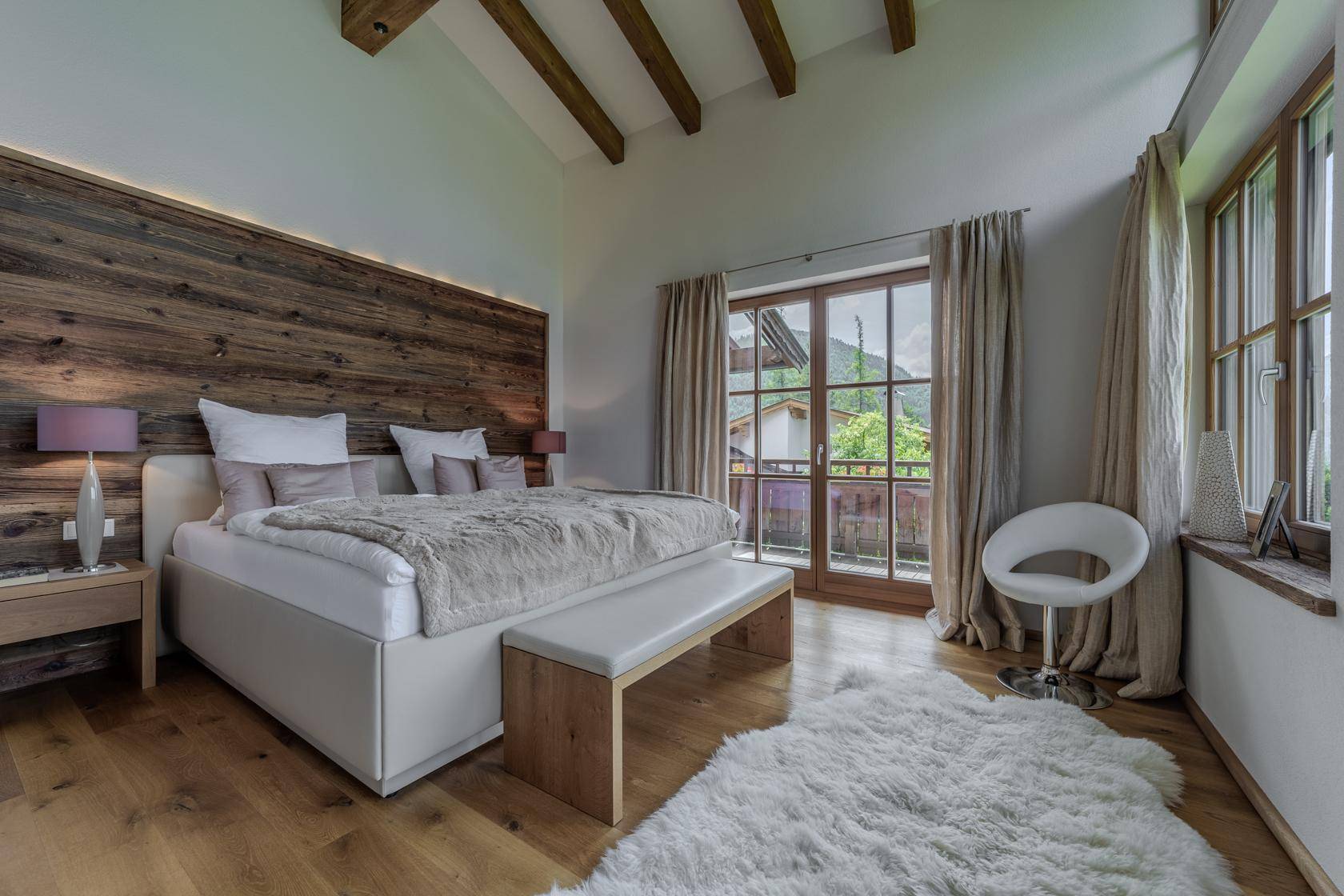 Gemütliches Schlafzimmer mit Holzwand, Balkonzugang und Blick auf die umliegende Natur.