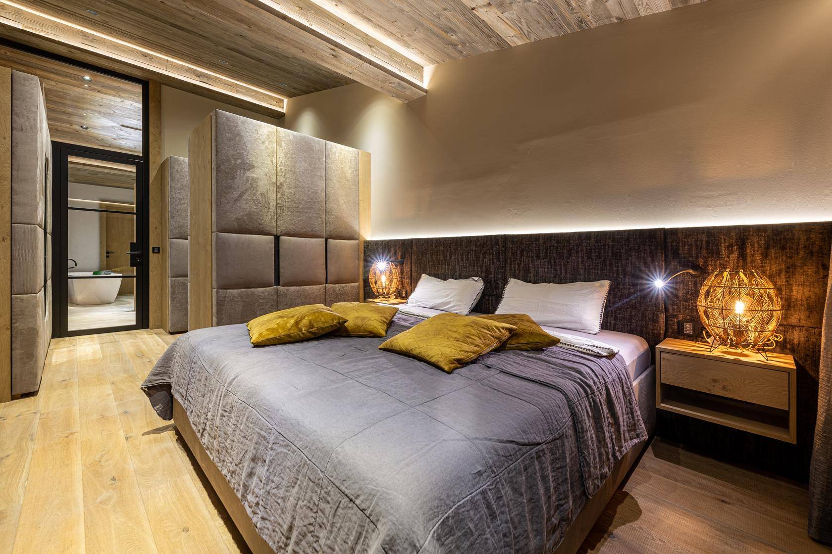Gemütliches Schlafzimmer mit Holzboden, gepolstertem Kopfteil und indirekter Beleuchtung.