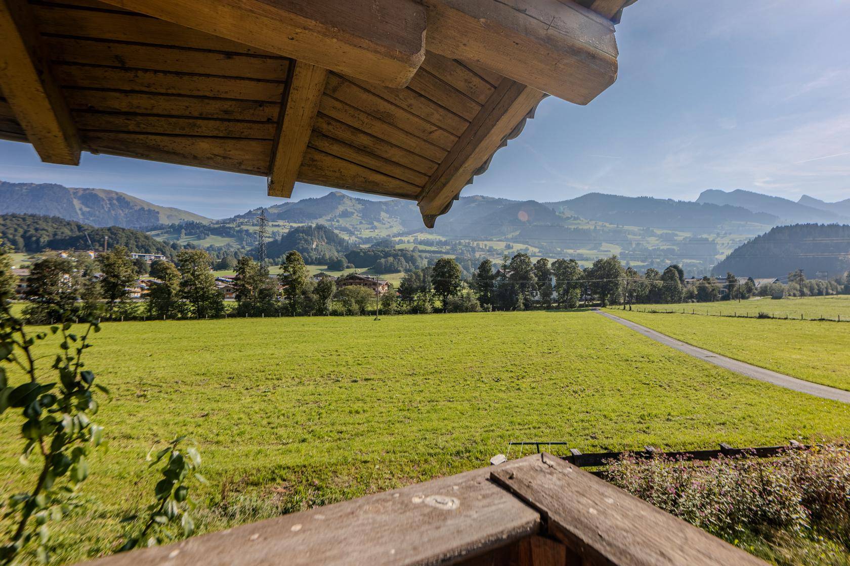 Blick vom Balkon auf weite grüne Felder und die umliegende Berglandschaft unter blauem Himmel.