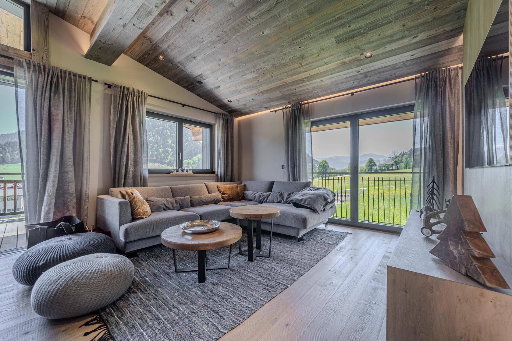 Gemütlicher Wohnbereich mit großem Ecksofa, Holzboden und weitem Blick auf die grüne Landschaft.