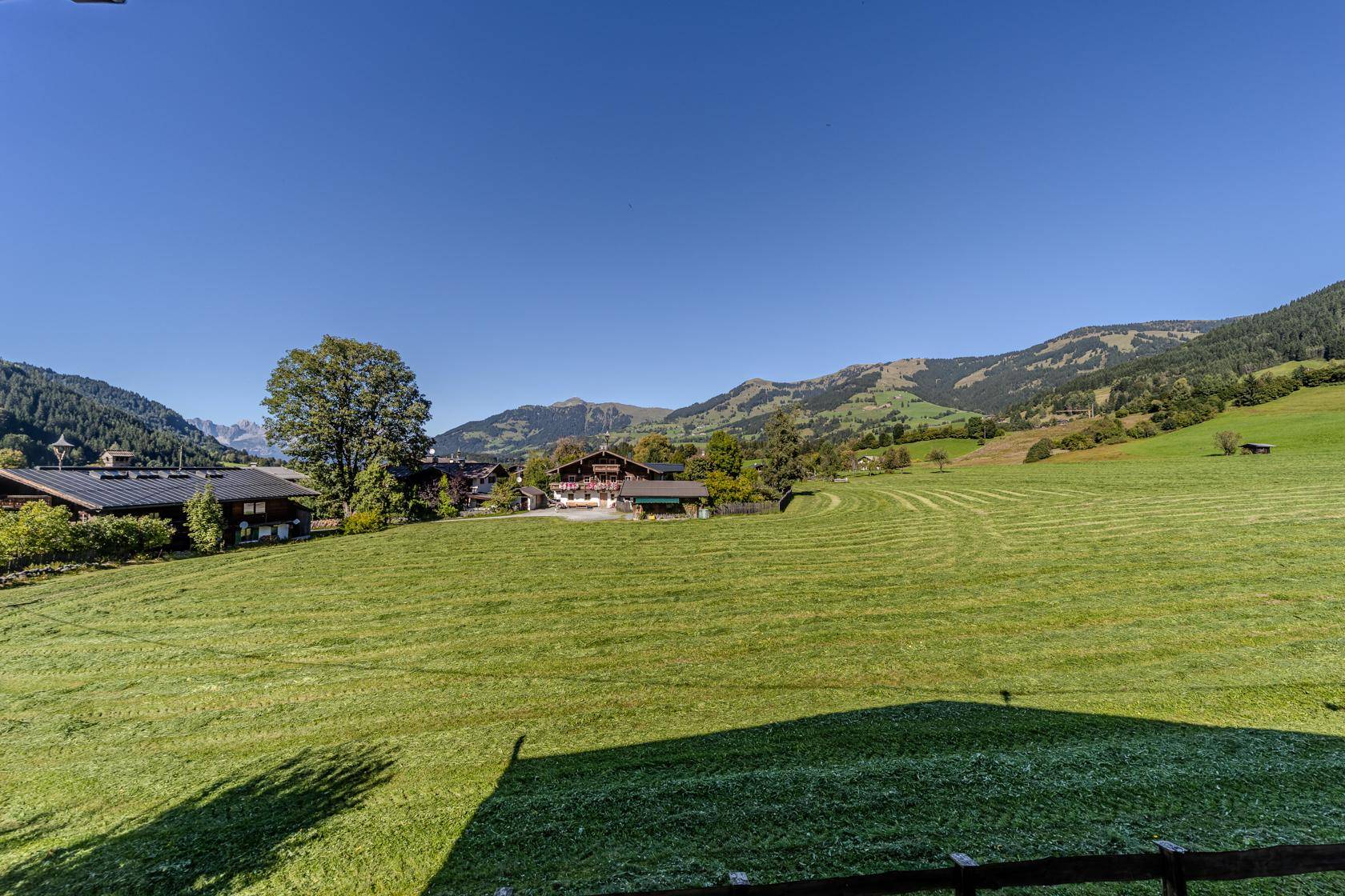 Weitläufiger Panoramablick über saftig grüne Wiesen und die beeindruckende Berglandschaft unter blauem Himmel.