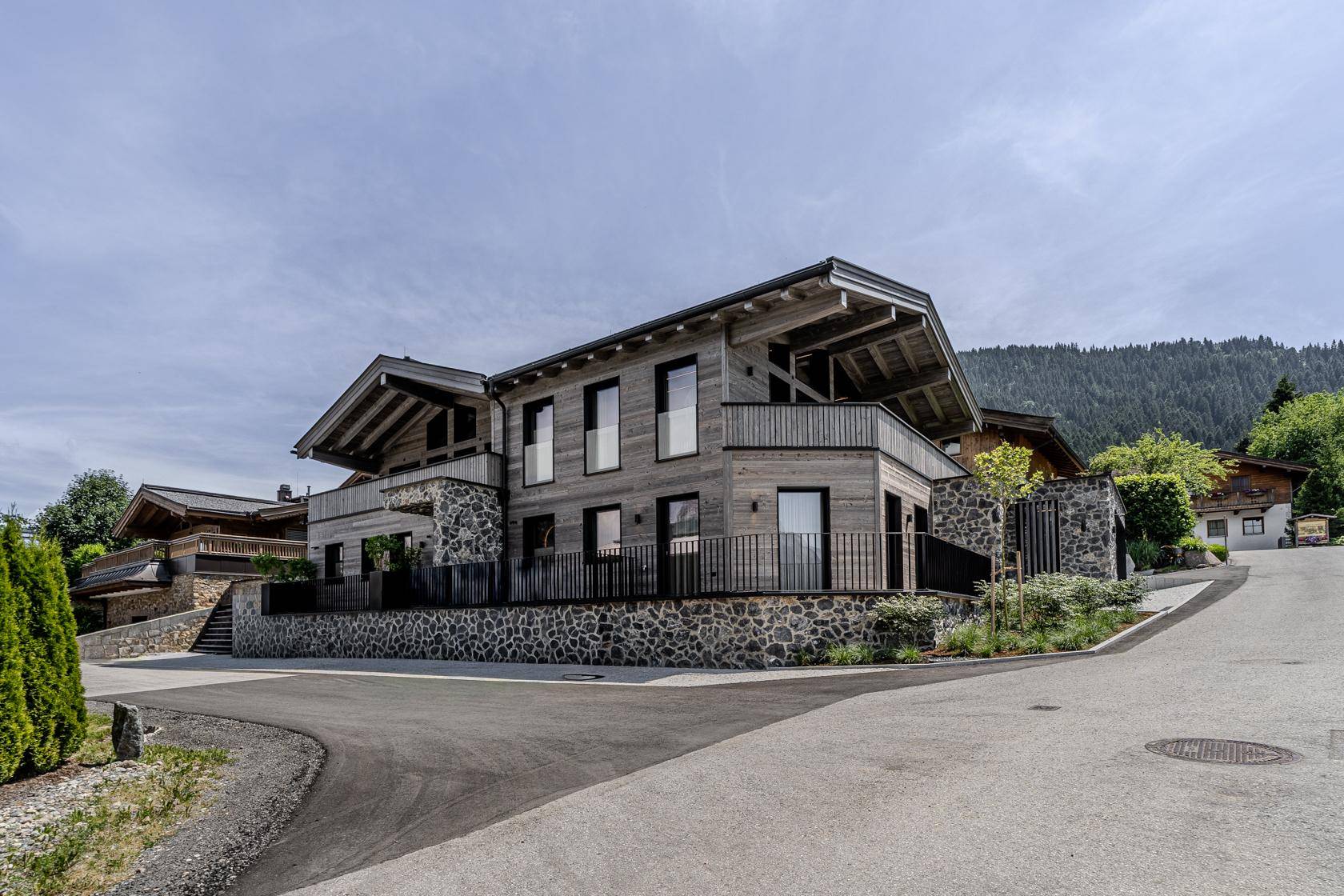 Exklusive Villa mit Holz- und Steinfassade, Balkonen und Blick auf die umliegende Berglandschaft.