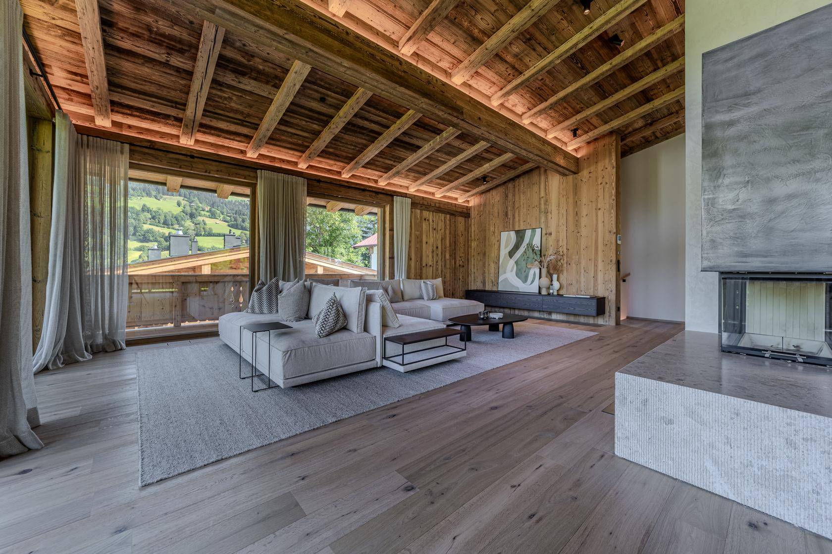 Gemütliches Wohnzimmer mit Holzwänden, Kamin und Blick auf die umliegende Berglandschaft.