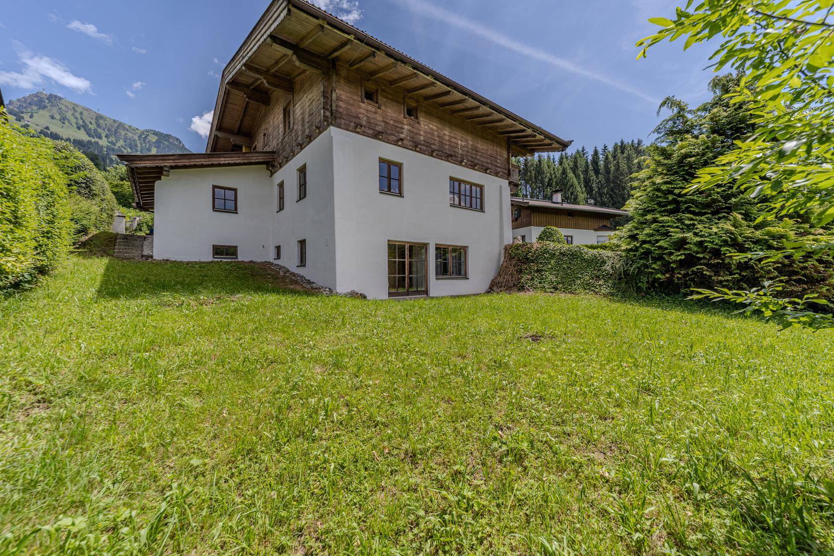 Das traditionelle Alpenhaus steht auf einem grünen Hügel mit Blick auf die umliegenden Berge.