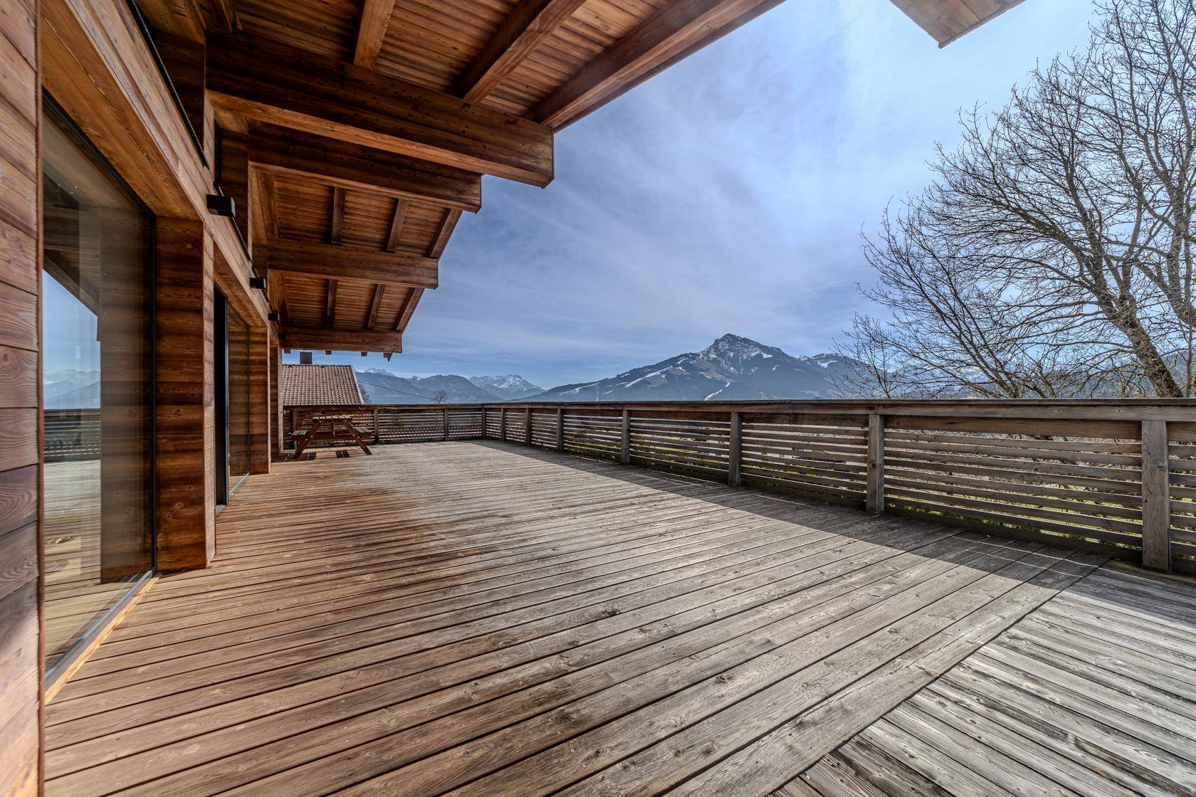Große Holzterrasse mit weitem Blick auf die umliegende Berglandschaft und viel Sonne.