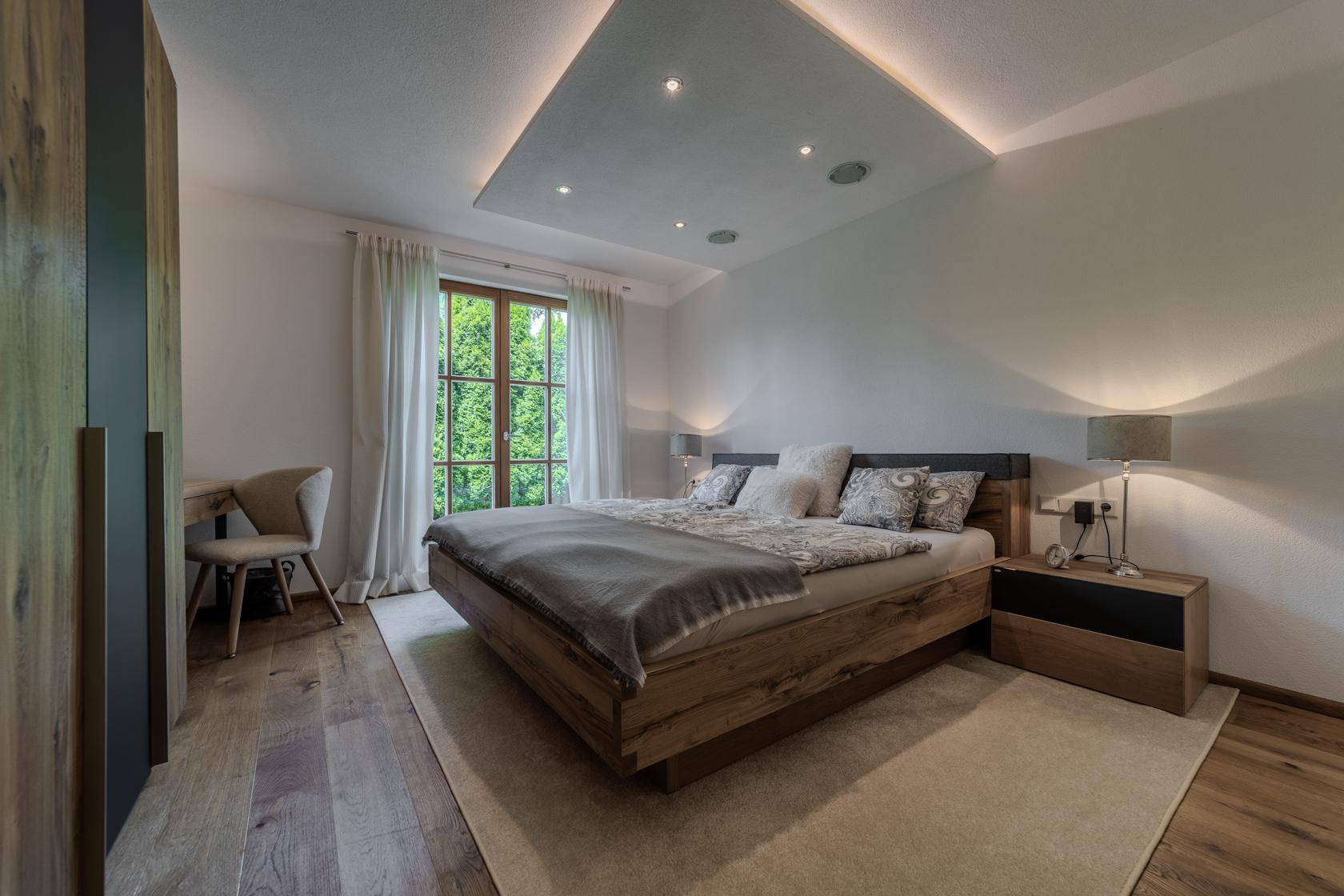 Modernes Schlafzimmer mit Holzbett, indirekter Beleuchtung und Blick ins Grüne.
