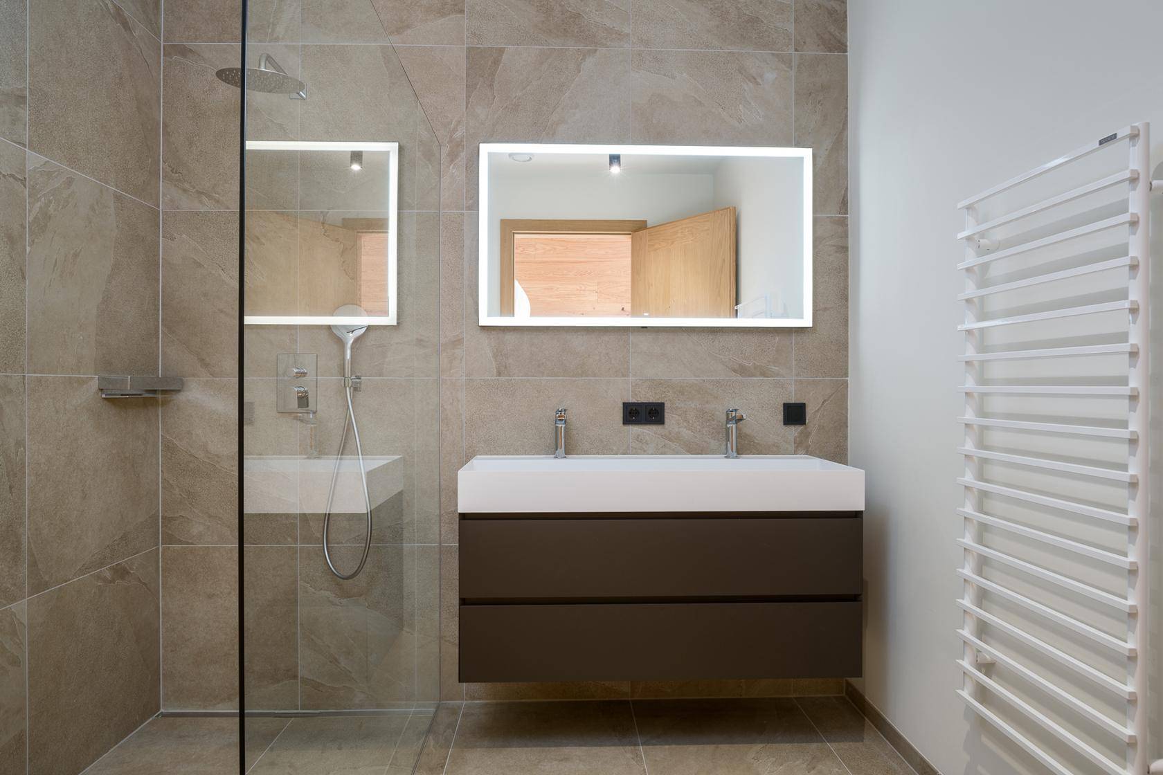 Modernes Badezimmer mit Doppelwaschbecken, großer Dusche und beleuchtetem Spiegel.
