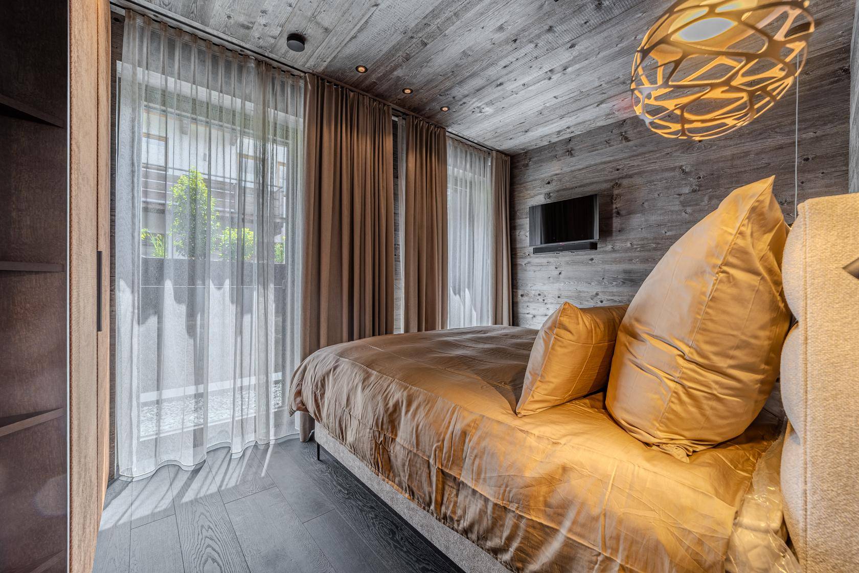 Helles Schlafzimmer mit Holzwänden, großem Bett und einem Fenster mit Blick ins Grüne.
